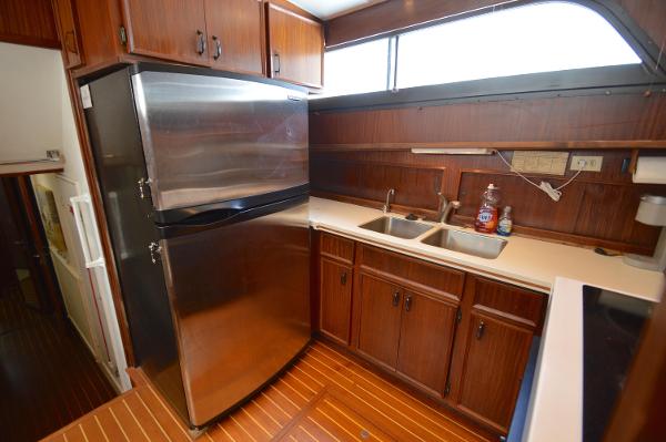 Interior view of a yacht kitchen with wooden cabinets, stainless steel fridge, and double sink.
