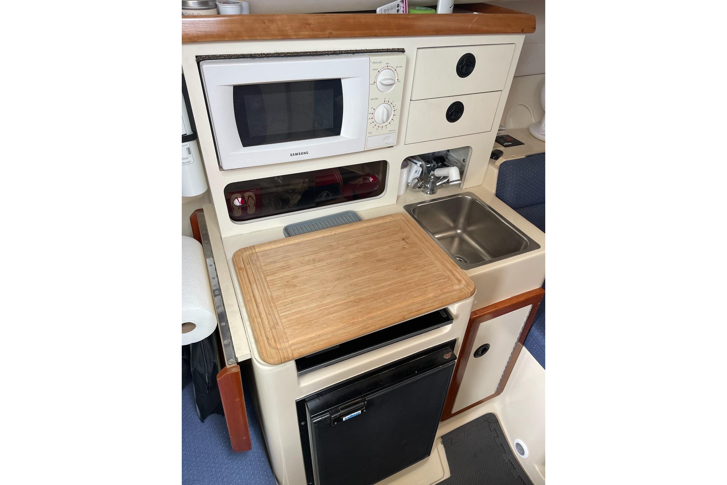 2003 Albin 28 Tournament Express galley with microwave, sink, and compact fridge.