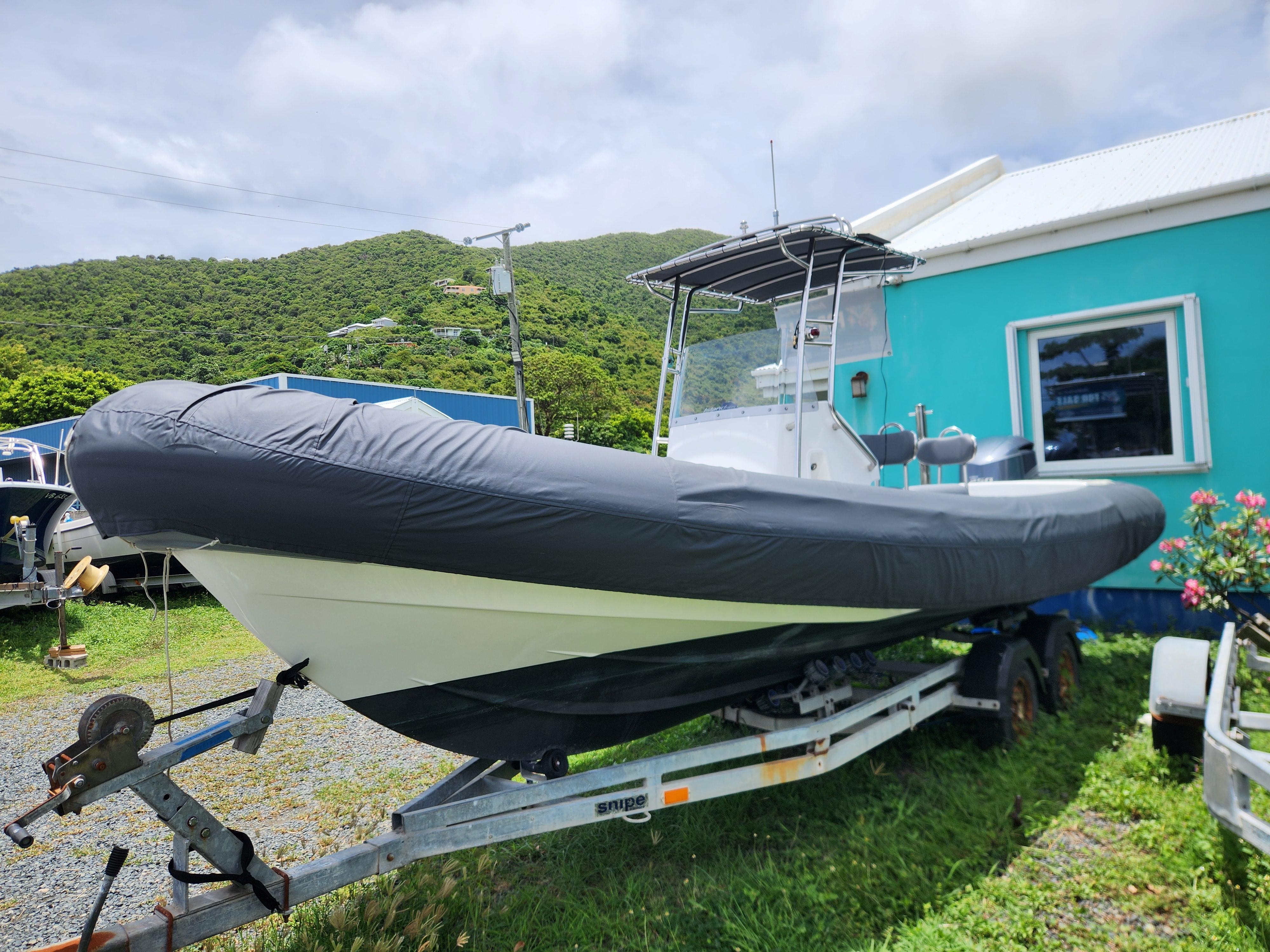 2023 Island RIBs 7.5 m boat on trailer, covered, near turquoise building and green hills.