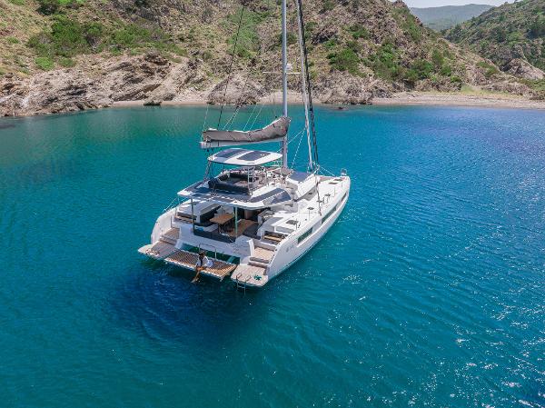 2025 Lagoon 51 ICONIC catamaran sailing in clear blue waters near rocky coastline.