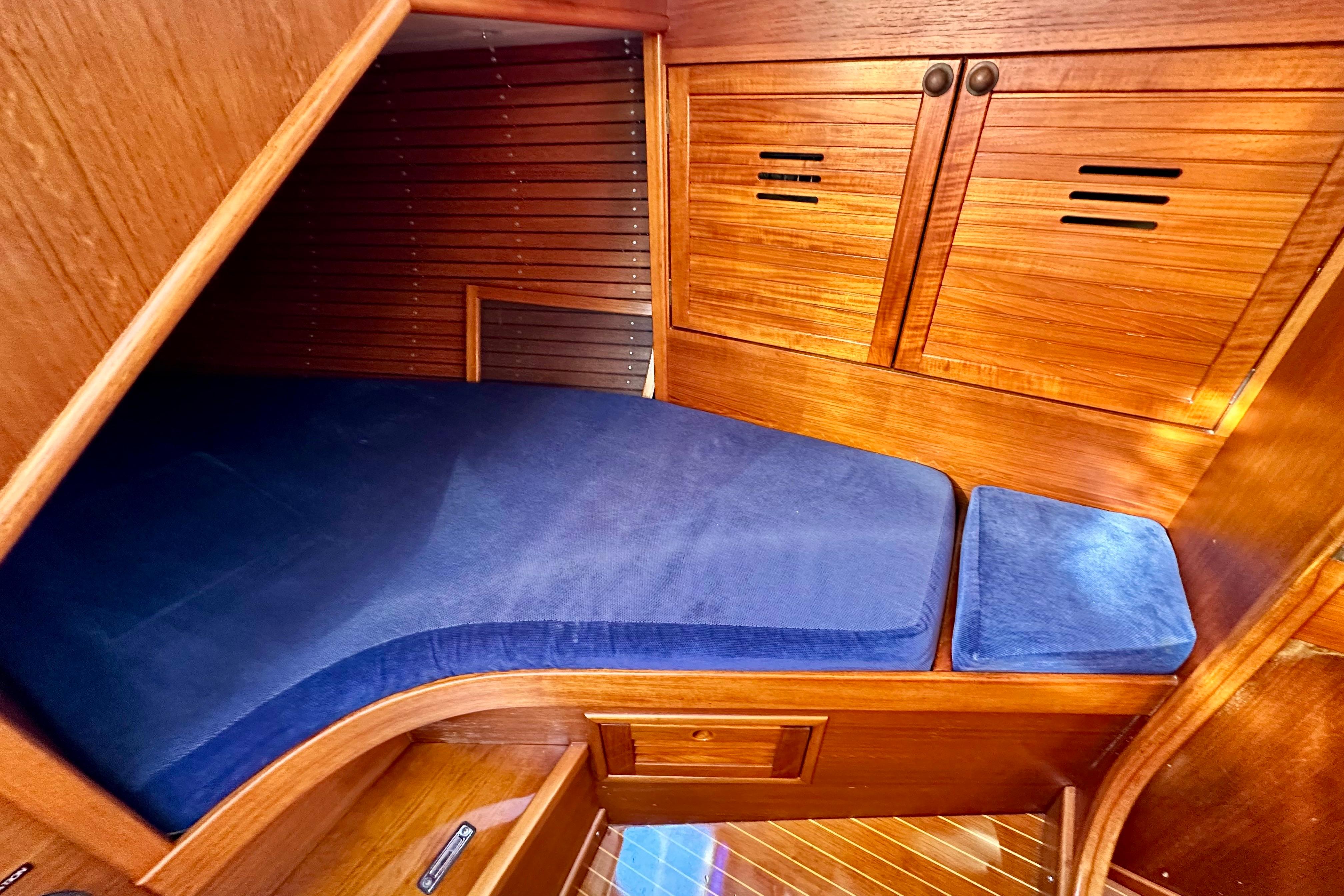 Cozy cabin interior of 1984 Jonmeri 40 sailboat with blue cushions and wooden finish.