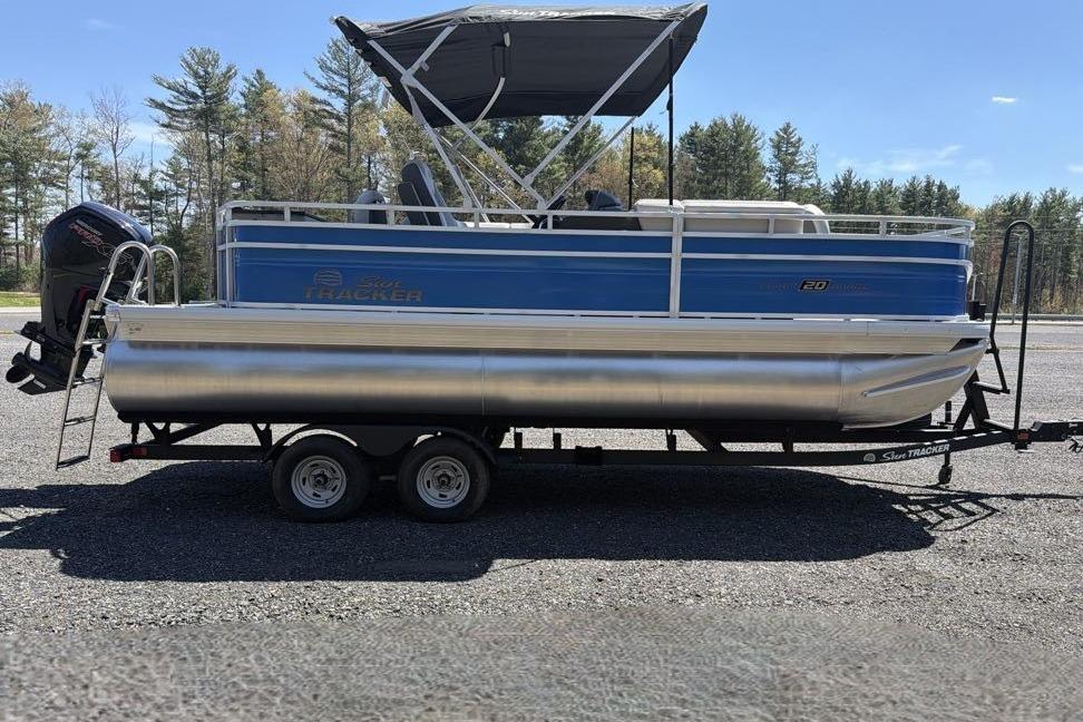 2026 Sun Tracker Fishin' Barge 20 DLX pontoon boat on trailer, parked outdoors.
