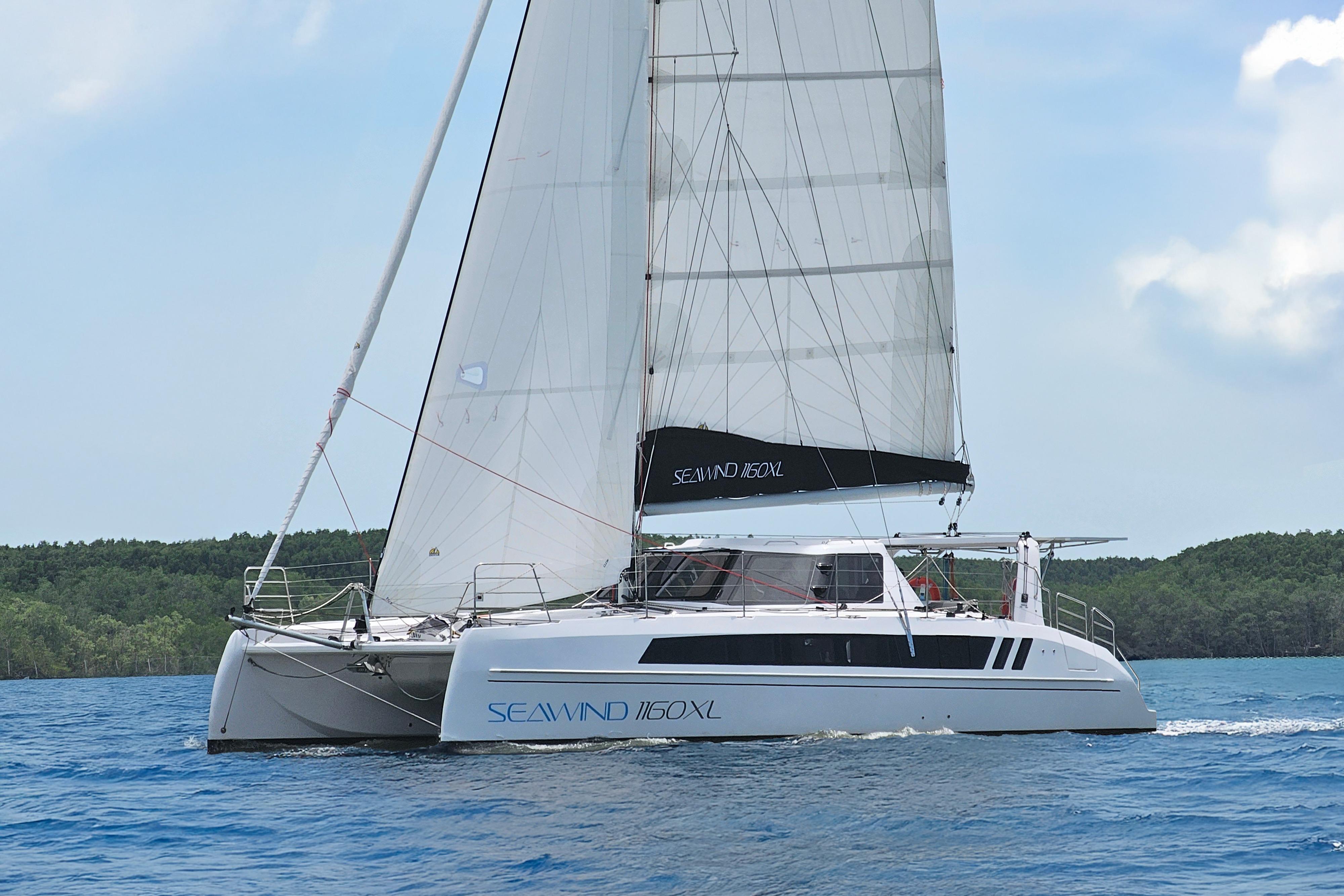 2026 Seawind 1160XL catamaran sailing on blue ocean with lush green shoreline.