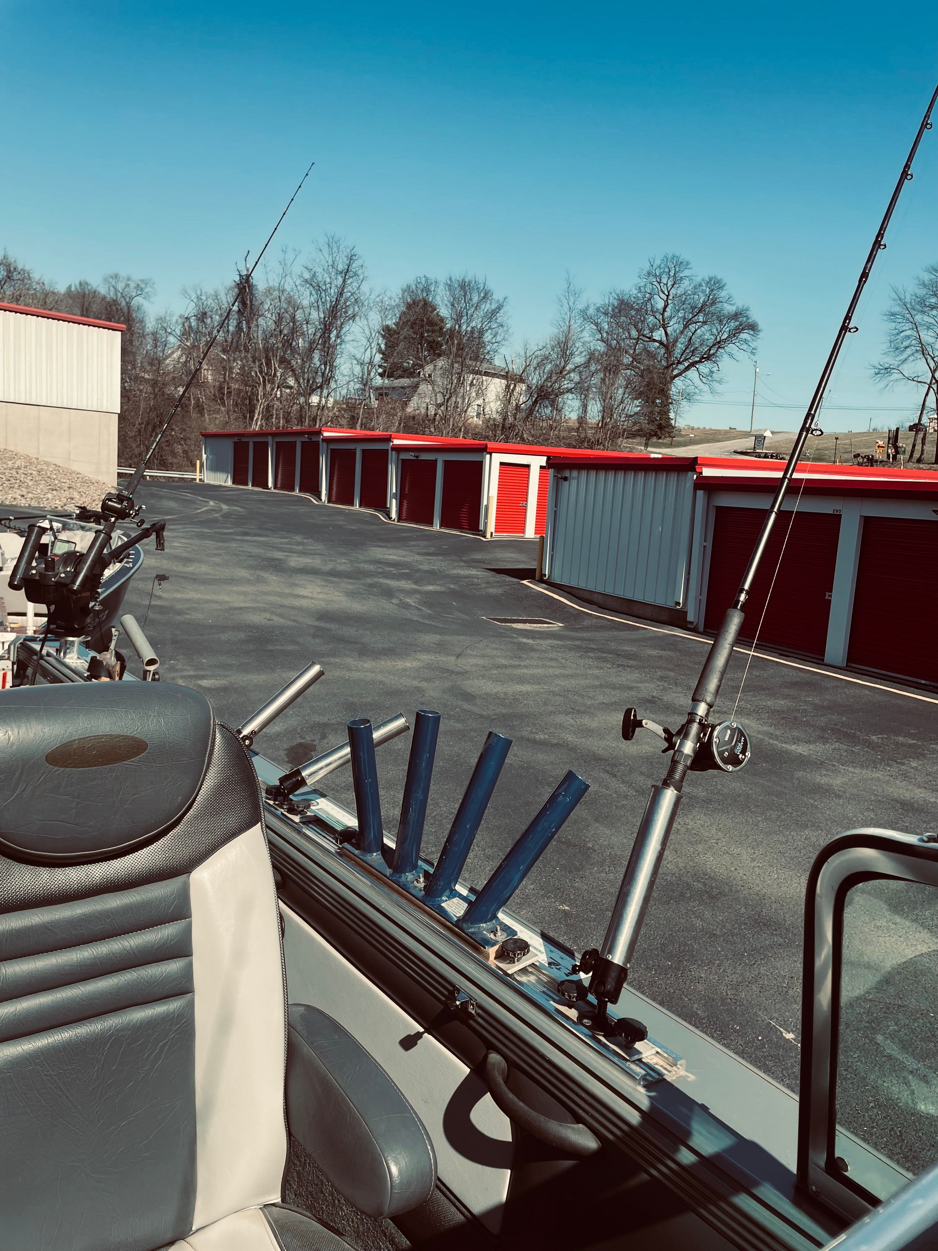 A 2012 Lund Baron boat with fishing rod holders, parked in front of red storage units.