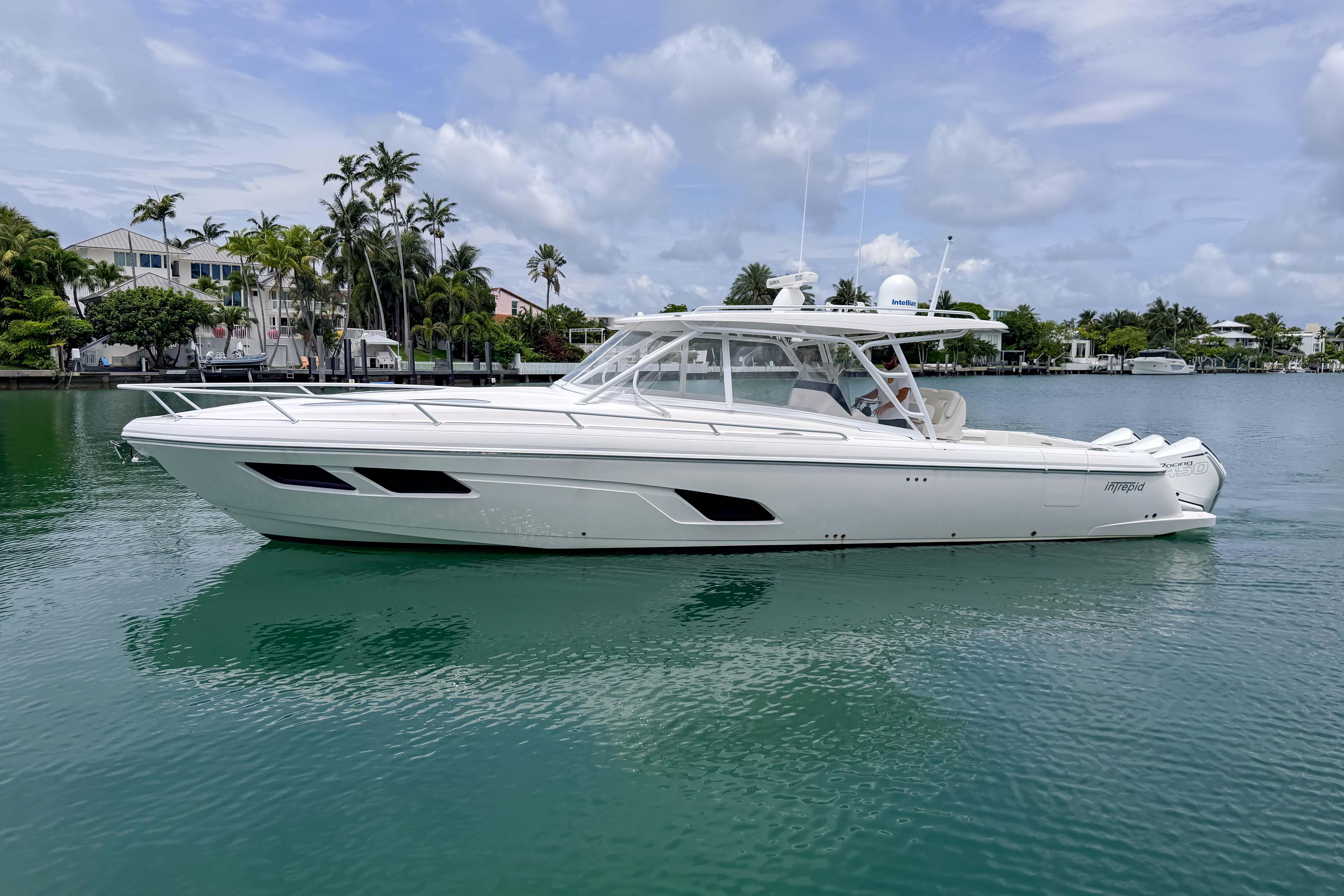 2021 Intrepid 409 Valor yacht cruising on calm waters, surrounded by lush greenery and luxury homes.