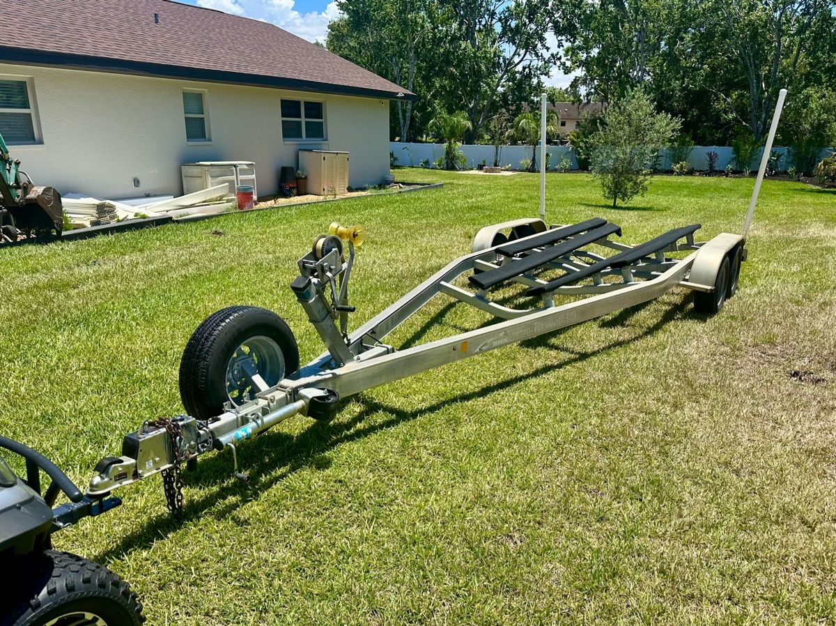 Boat trailer on grass in front of a house, ready for transport.
