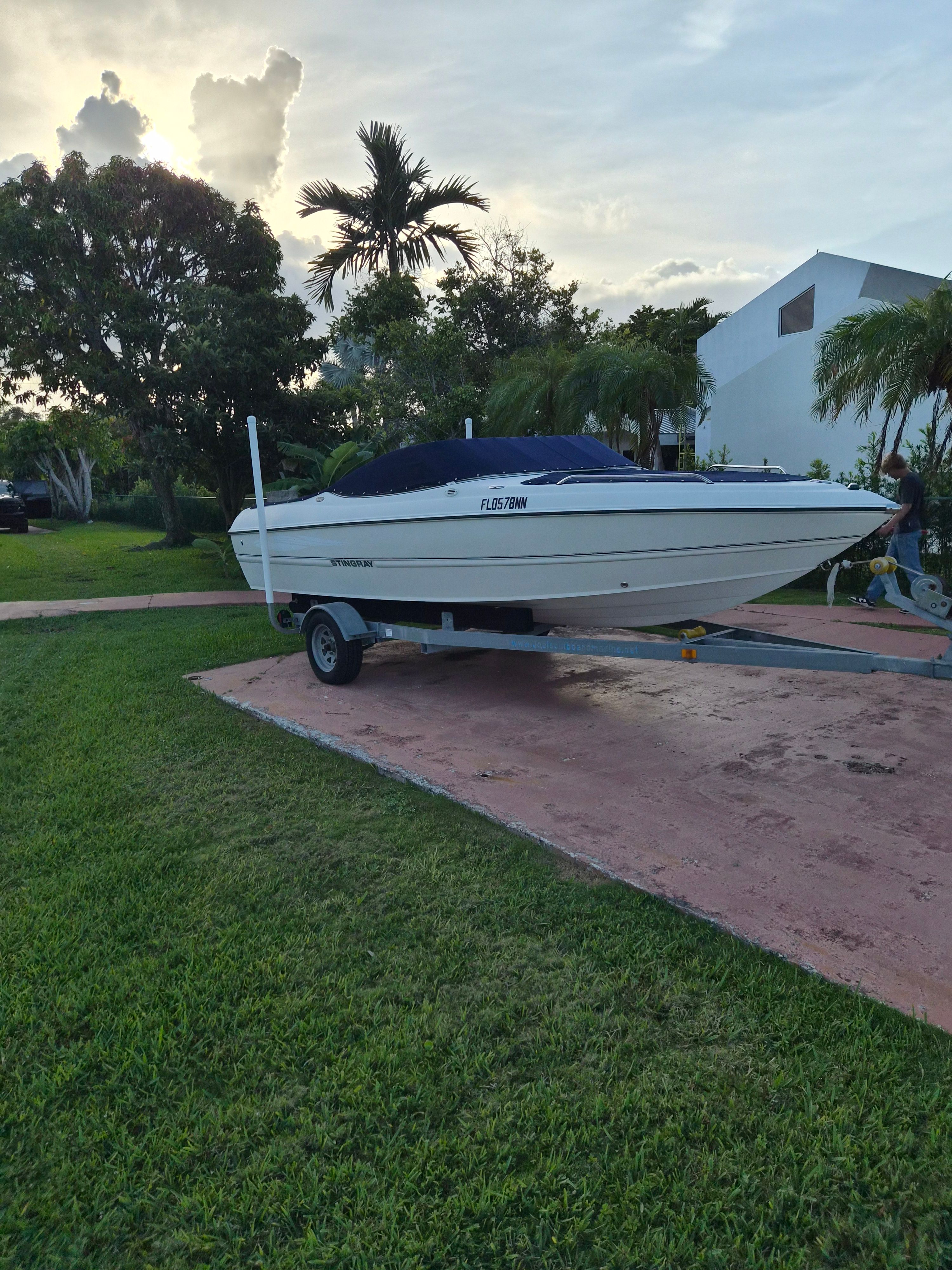 A white boat on a trailer on a lawn, surrounded by trees.