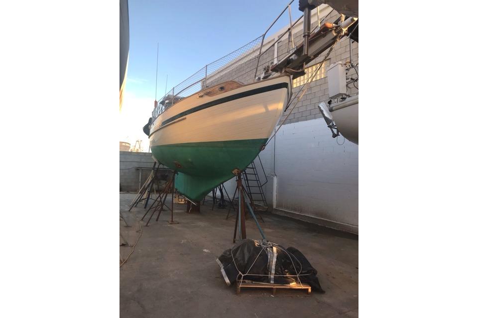 1978 Tayana 37 sailboat on dry dock, green hull, white upper, in a shipyard.