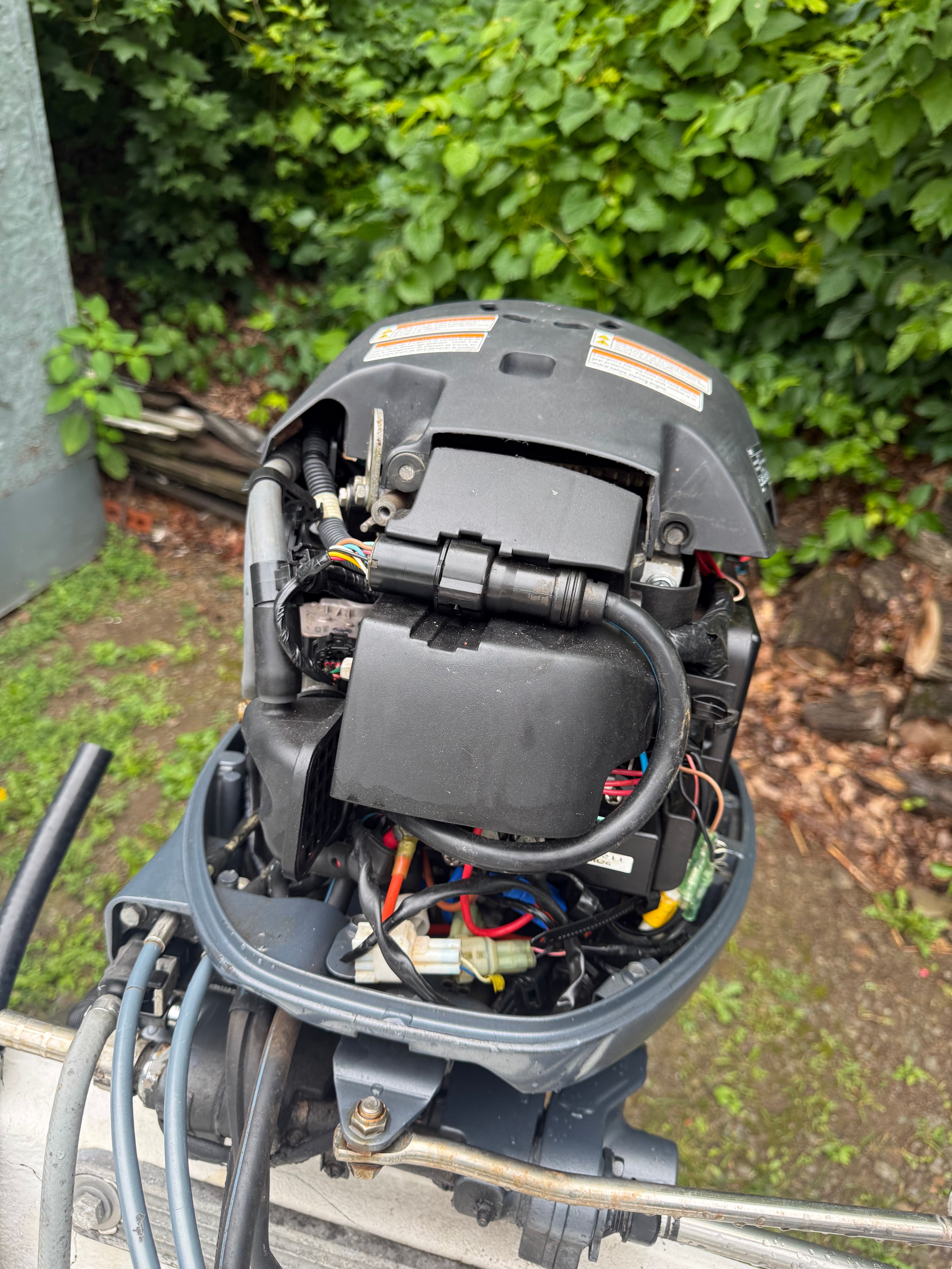 An outboard motor with exposed wires and components, surrounded by green vegetation.