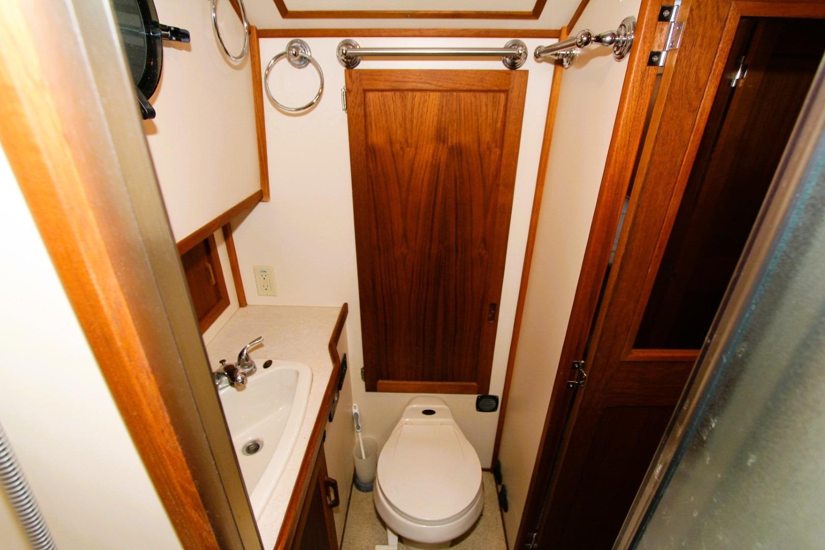 Compact bathroom in a 2002 Nordic Tug 37, featuring a sink, toilet, and wooden cabinetry.