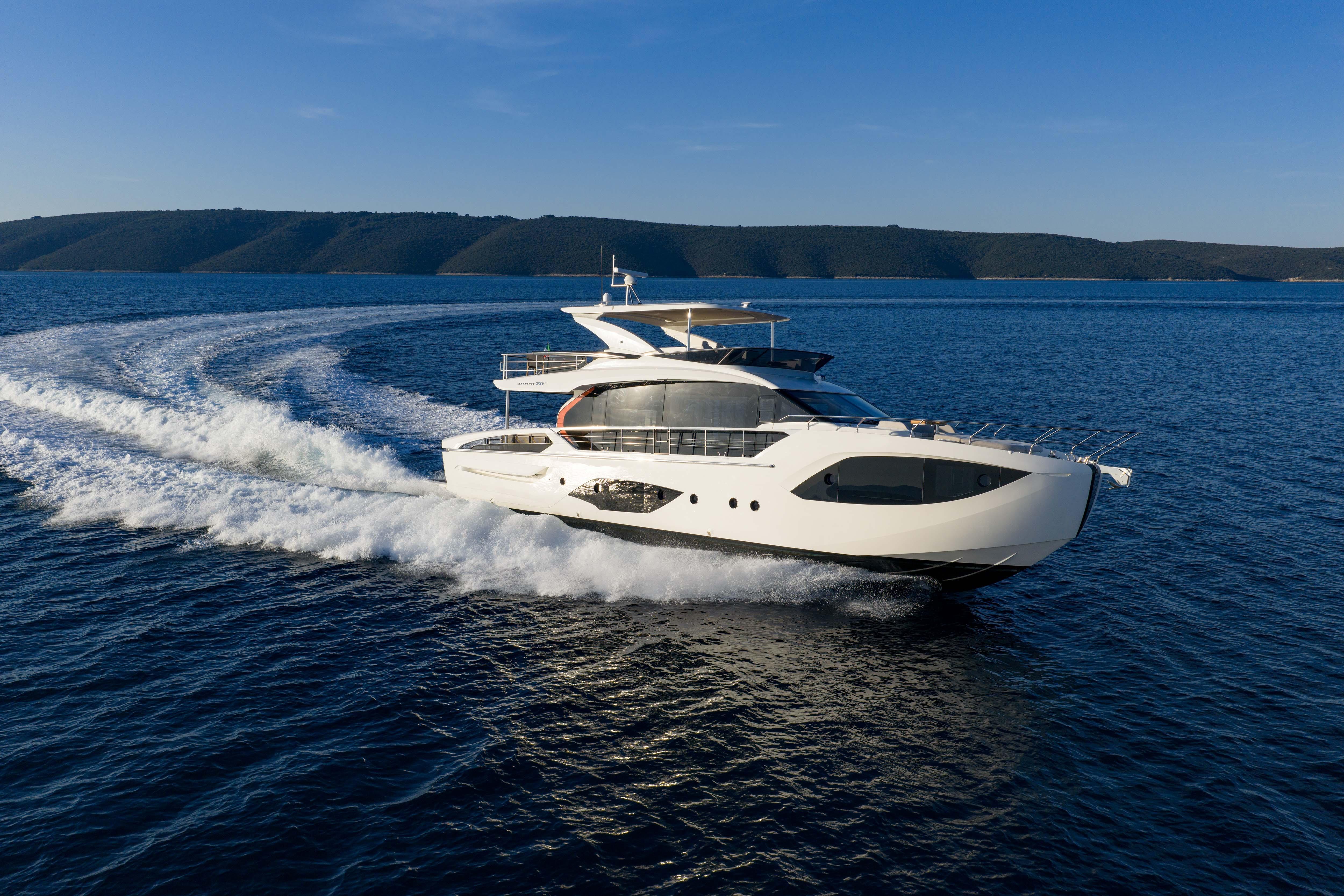 A luxurious yacht speeds across the blue sea, with a coastline in the background.