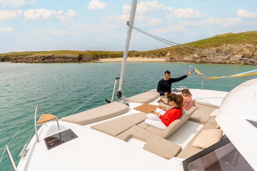 Family relaxing on 2026 Fountaine Pajot NEW 41 catamaran near scenic coastline.
