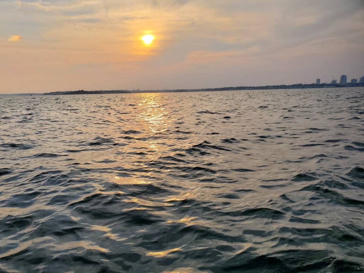 Sunset over calm water with distant buildings on the horizon.
