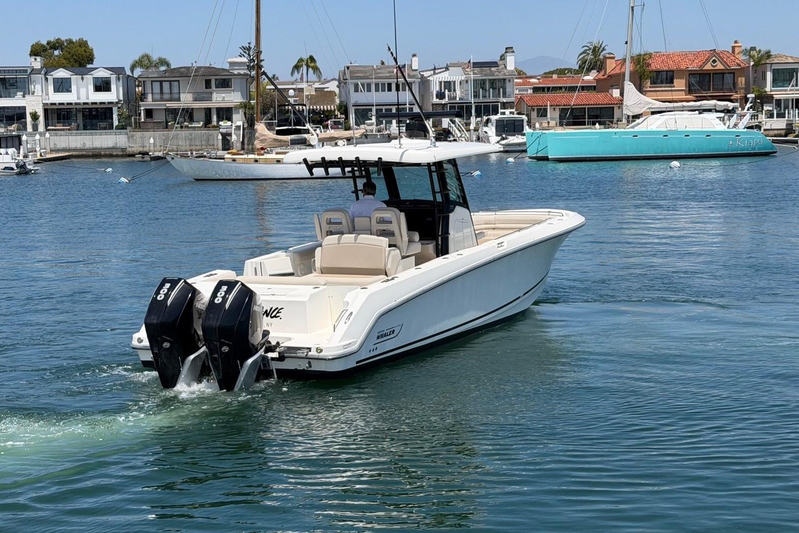 2021 Boston Whaler 330 Outrage boat cruising in a marina with waterfront homes.