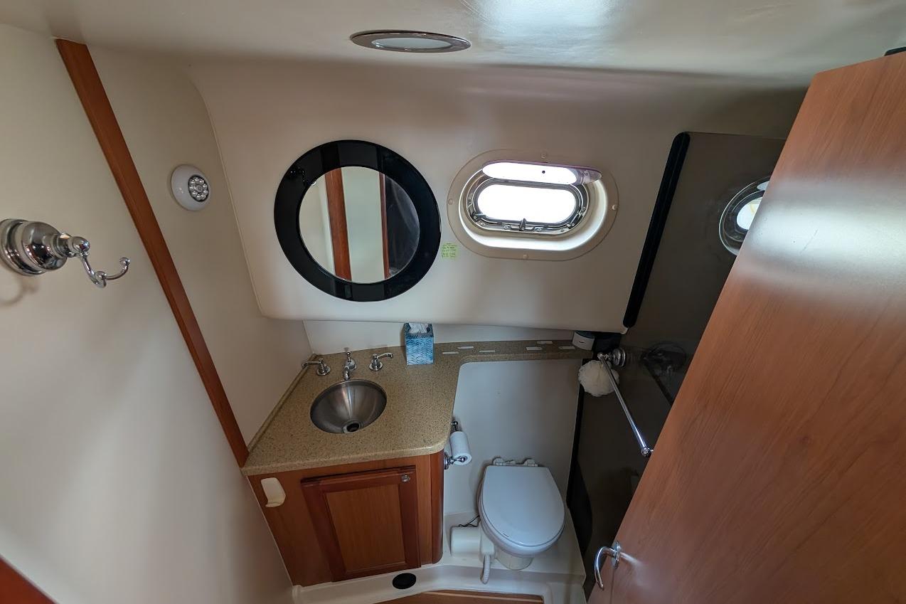 2008 Mainship 38 yacht bathroom with sink, toilet, mirror, and porthole window.