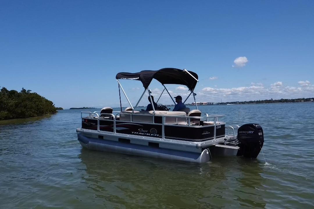 2017 Sun Tracker Bass Buggy 18 DLX pontoon boat on calm water under clear blue sky.