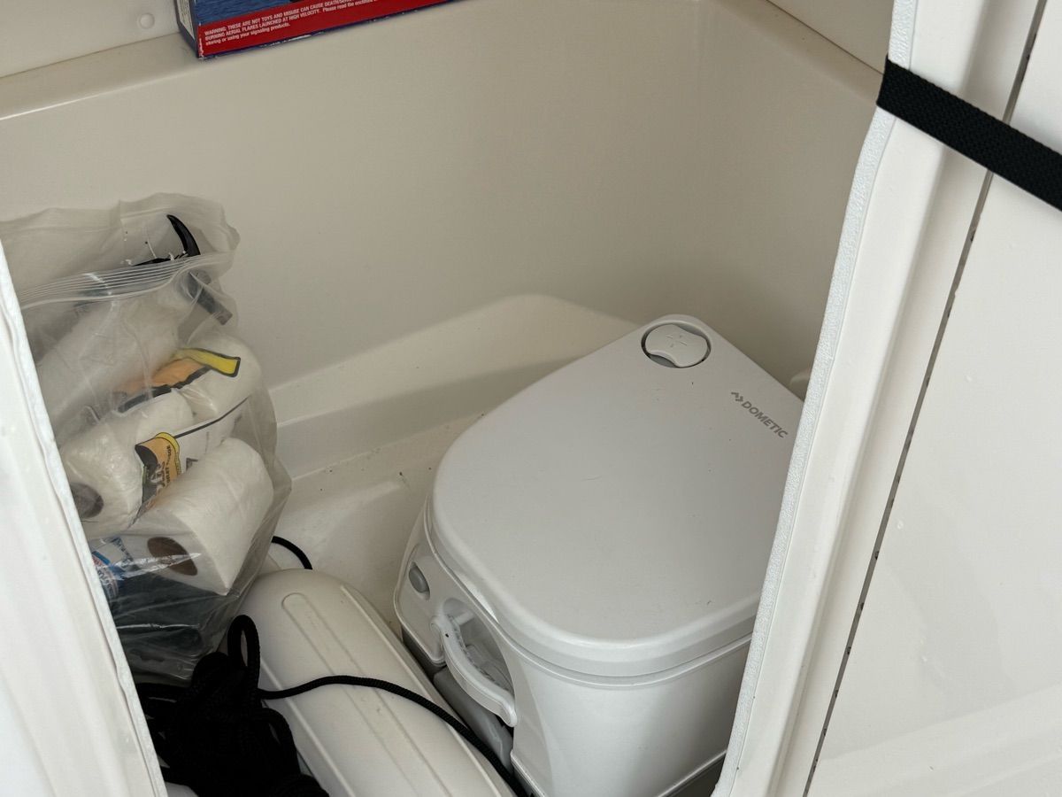 A compact toilet area with a portable toilet and storage for toilet paper.
