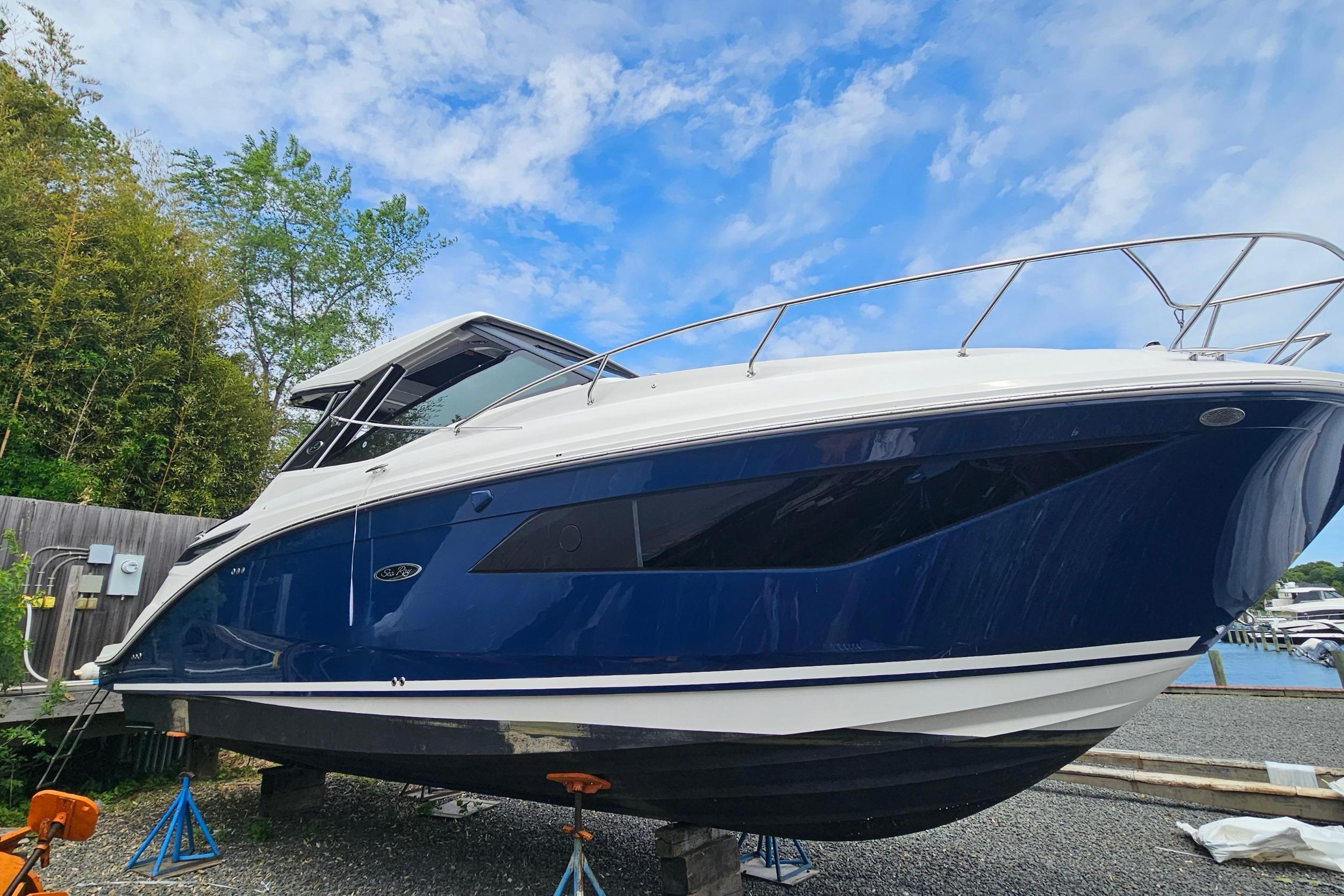 2023 Sea Ray Sundancer 320 boat on stands, blue hull, clear sky background.