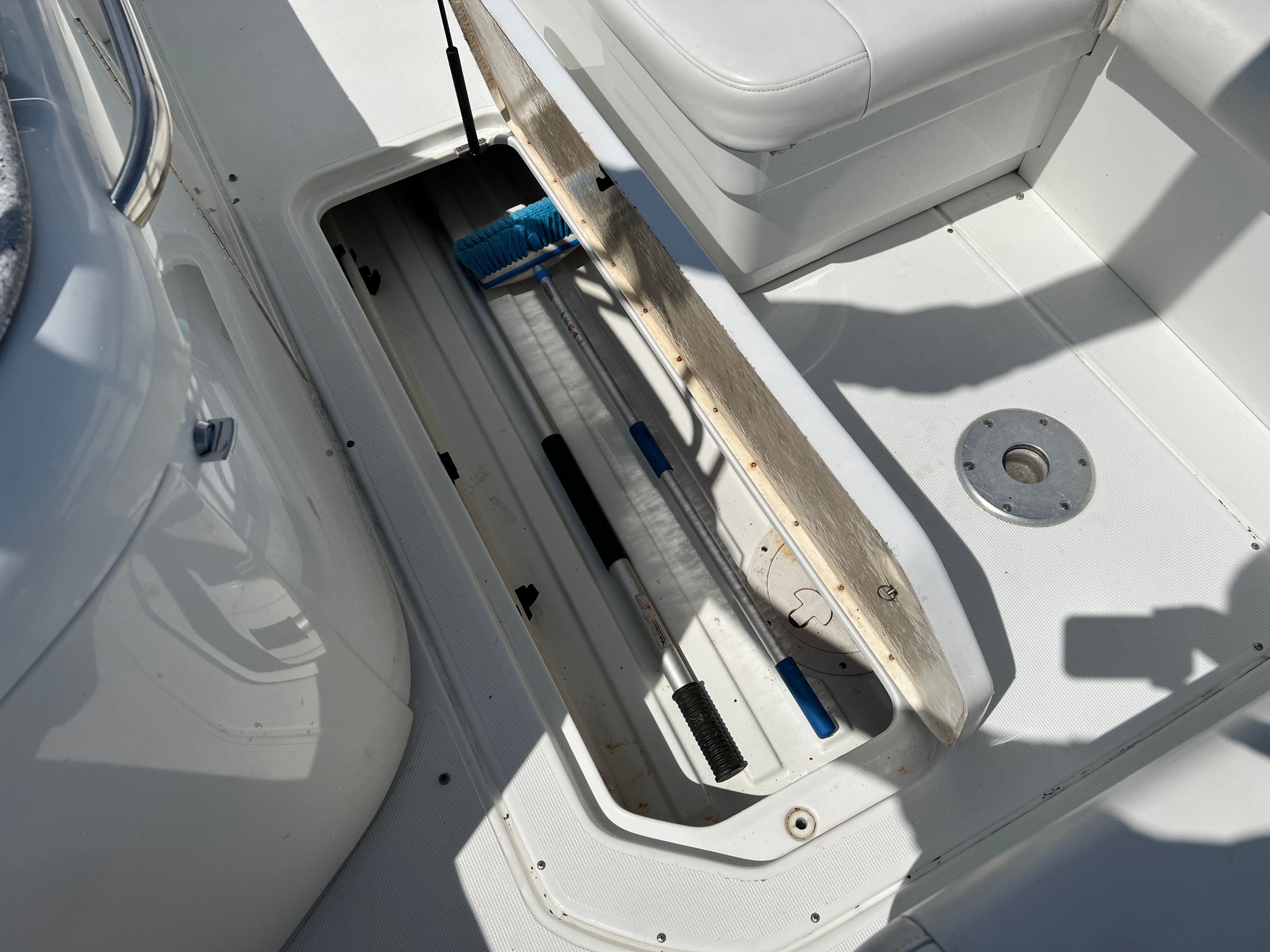 An open storage compartment on a boat with cleaning tools and a white seat.