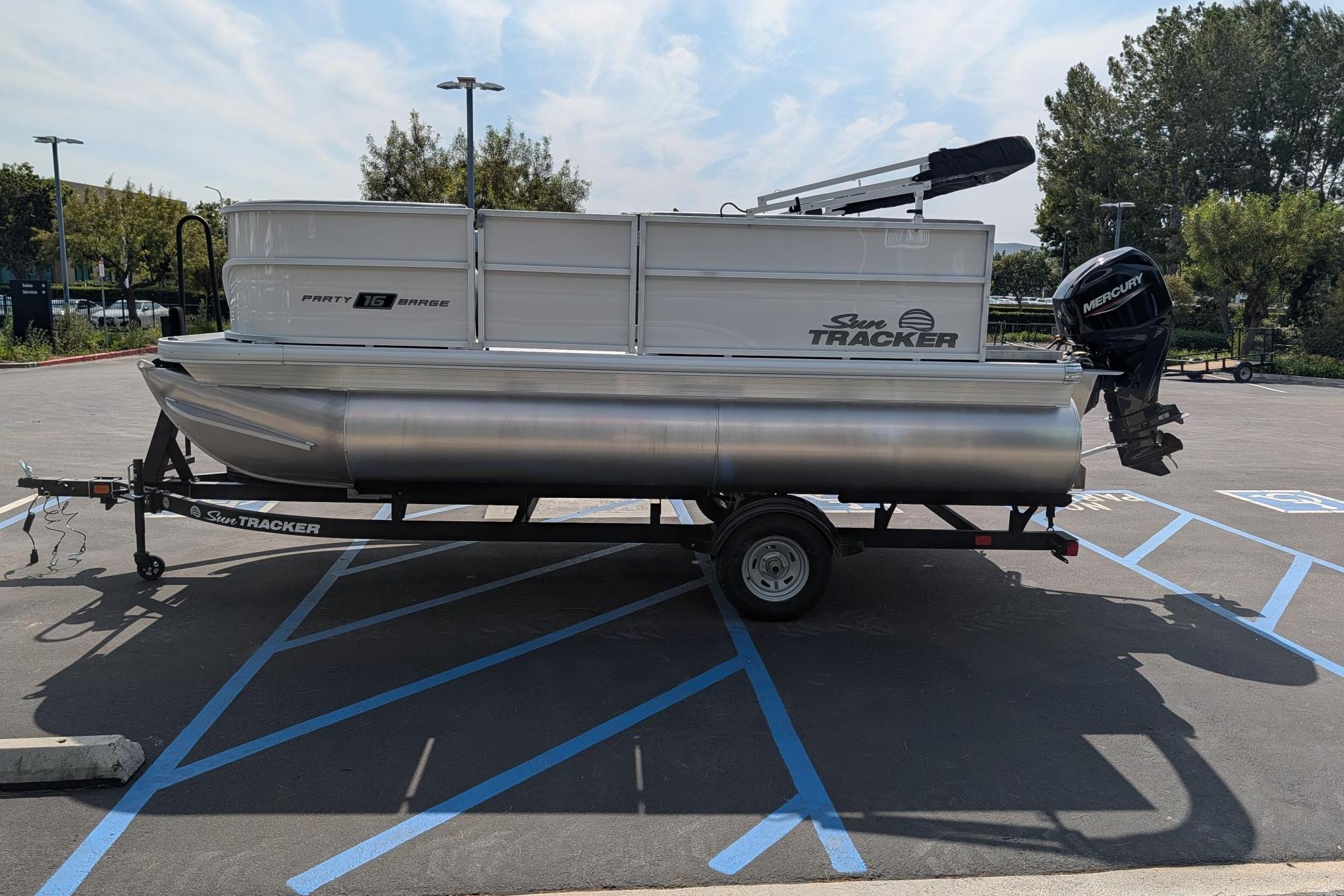 2026 Sun Tracker Party Barge 16 DLX pontoon boat on trailer in parking lot.