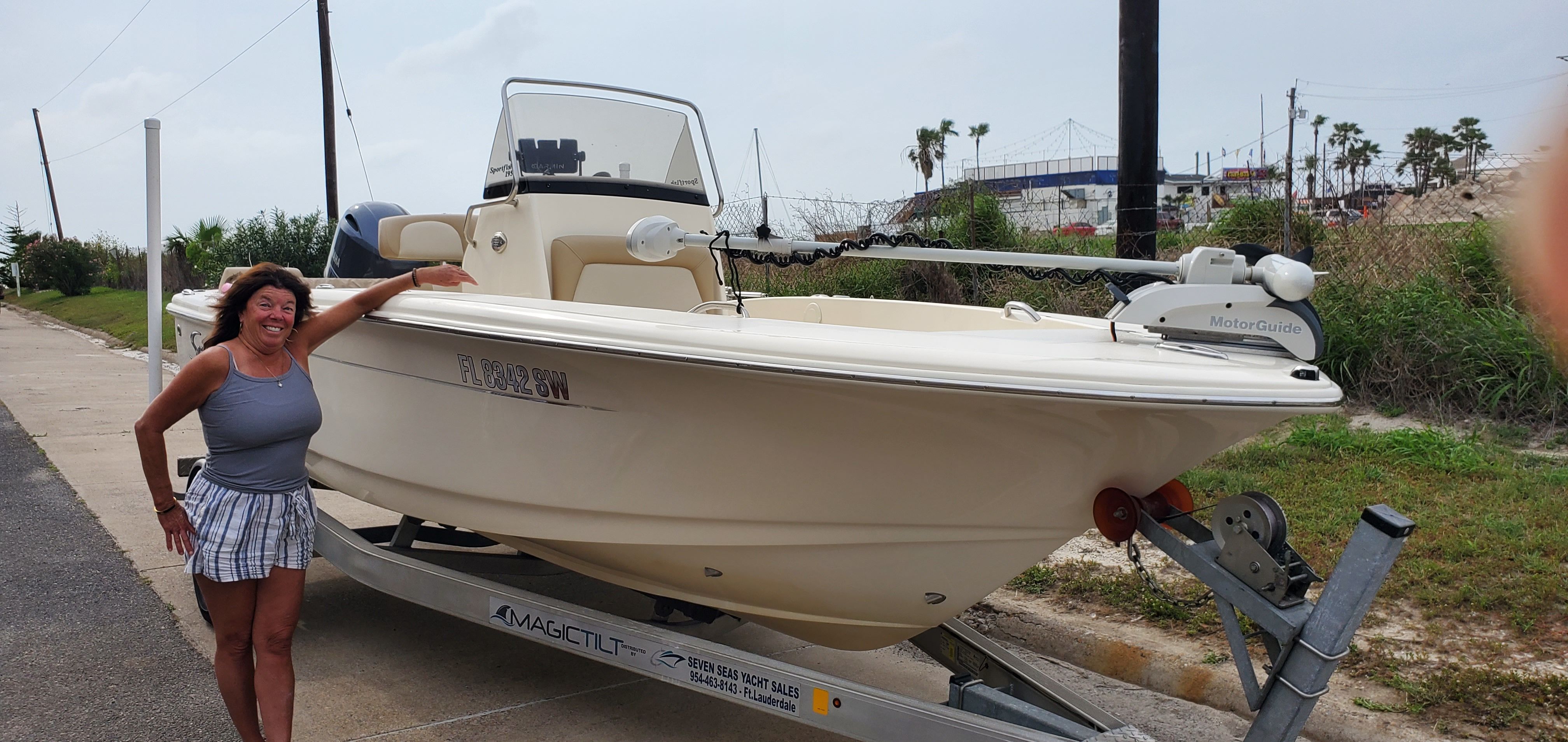 A woman stands next to a Scout 195 Sportfish boat on a trailer.