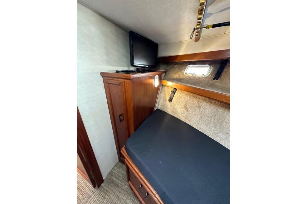 1985 Egg Harbor 33 Sedan cabin interior with bed, TV, and wooden cabinet.