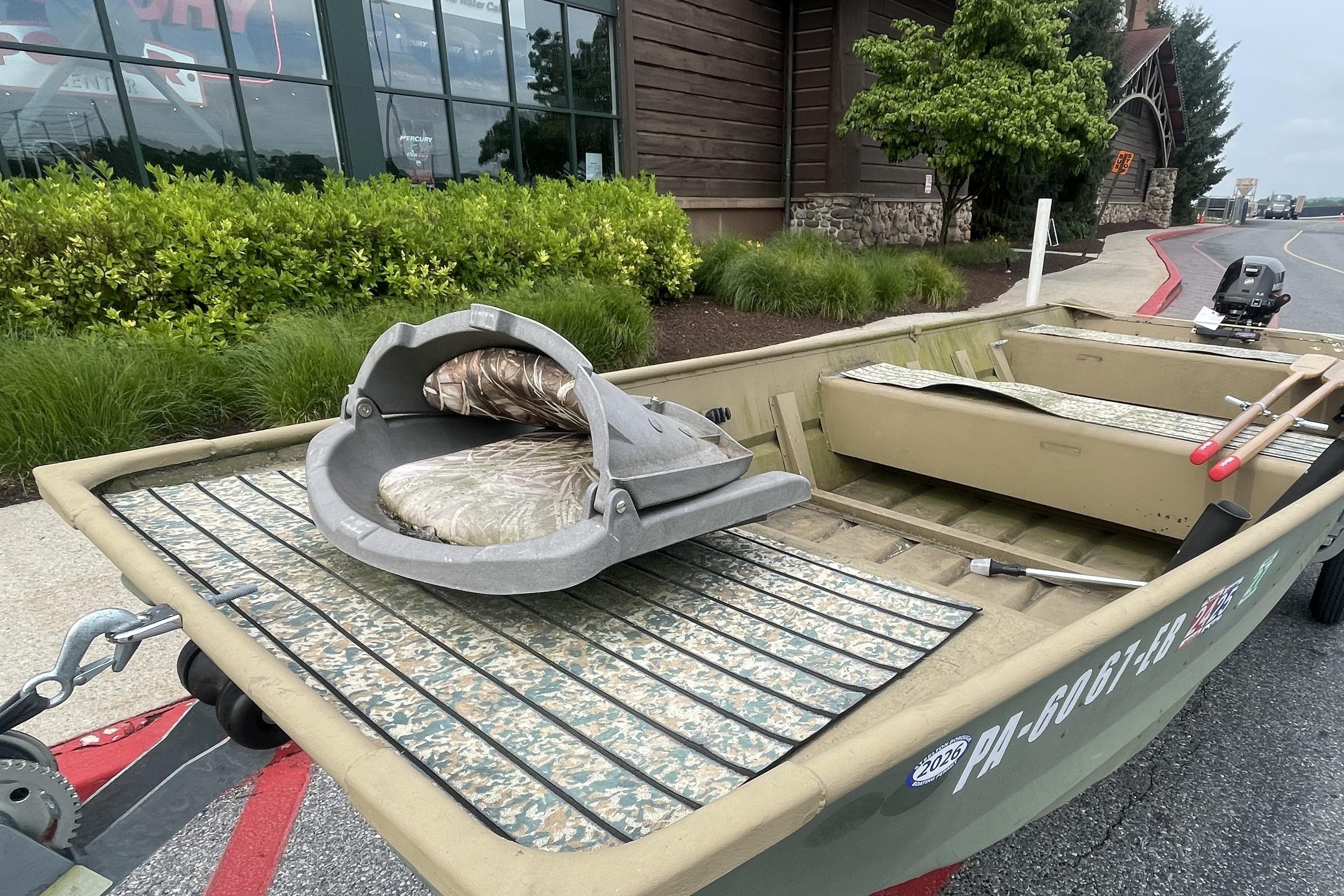 1986 Landau 1664 Jon boat with camouflage seating, parked outside a building.