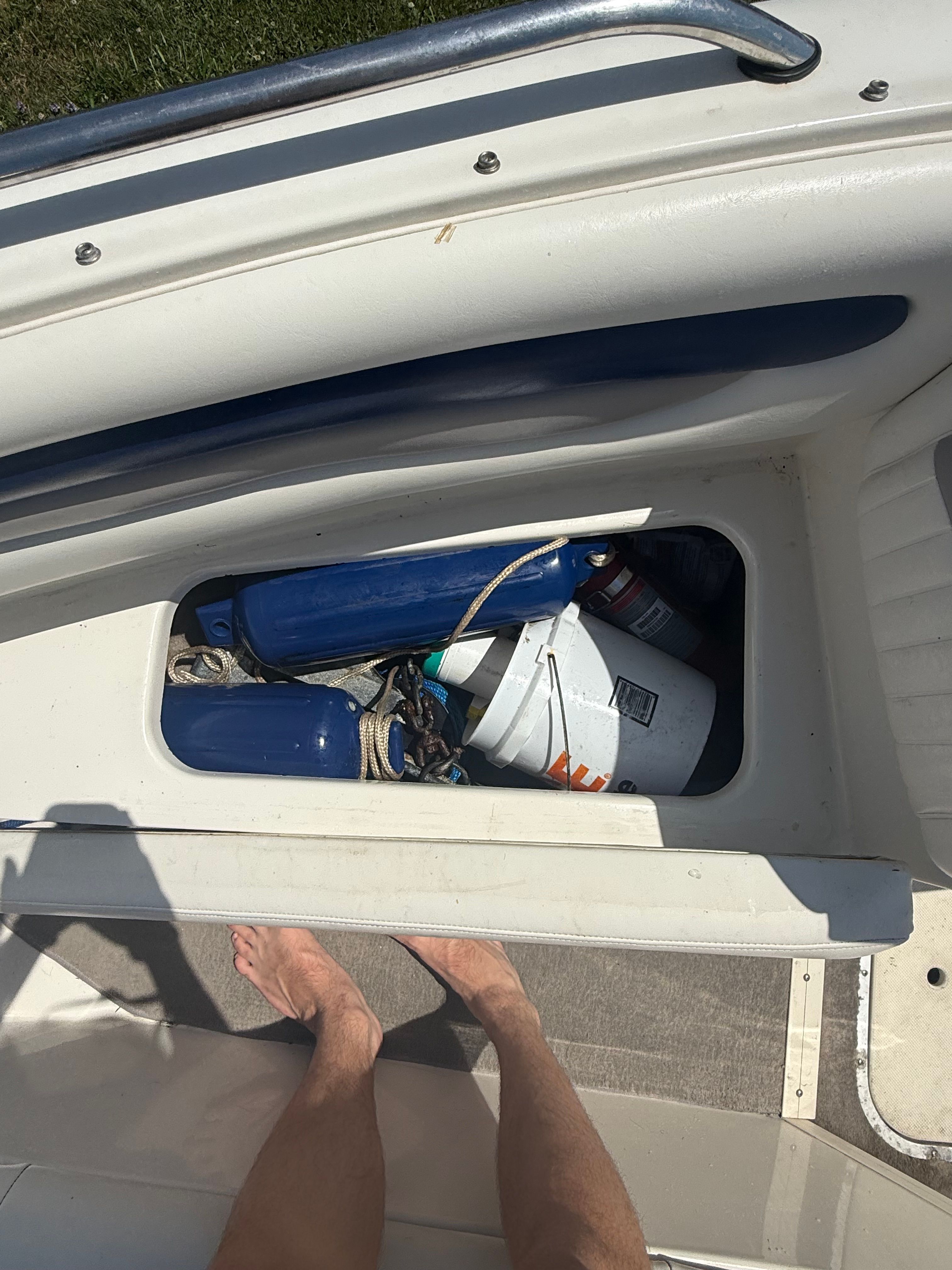 An open storage compartment on a boat with blue fenders and a white bucket.