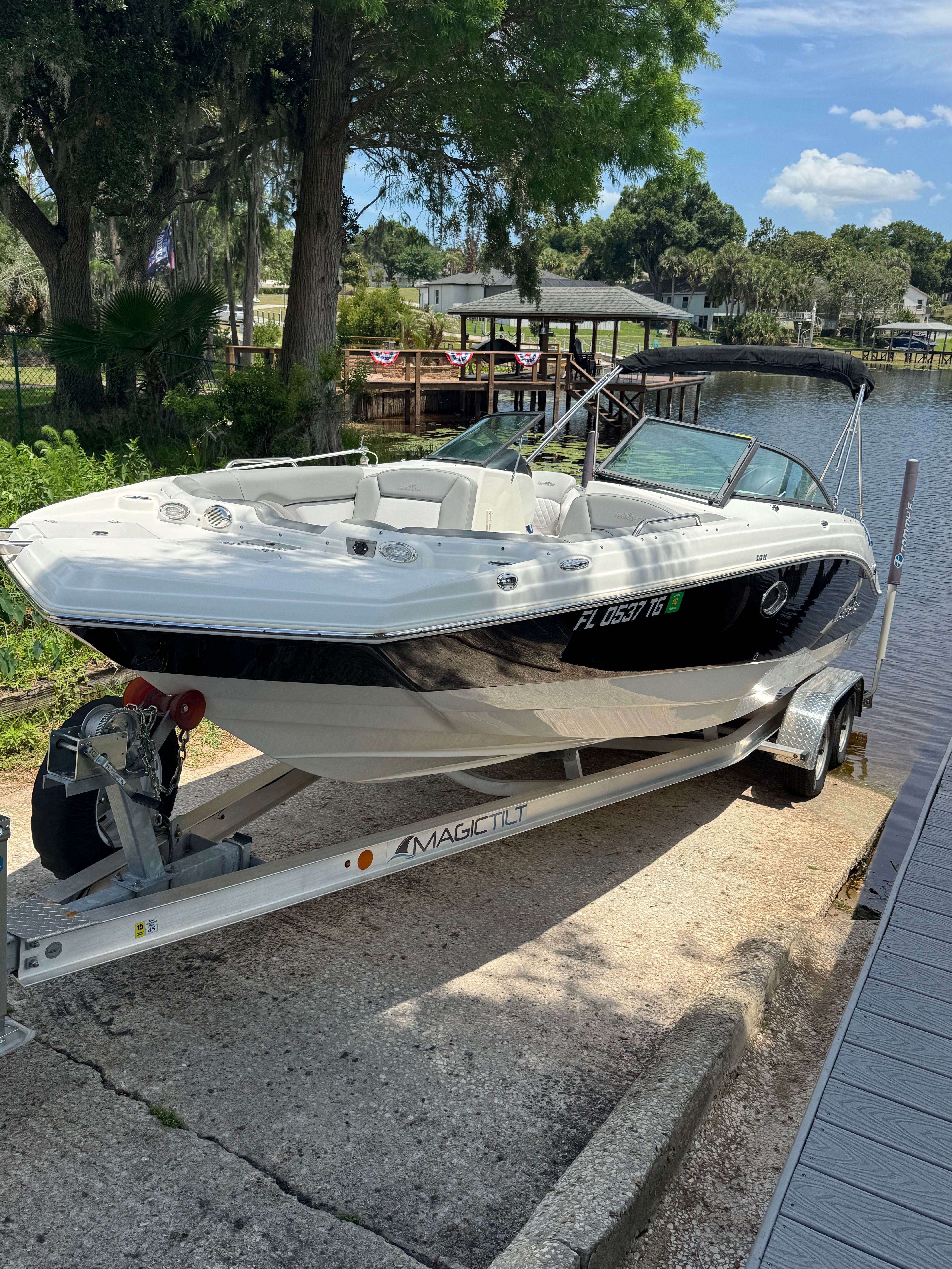 A white 2022 NauticStar 243 DC boat is on a trailer beside a calm river.
