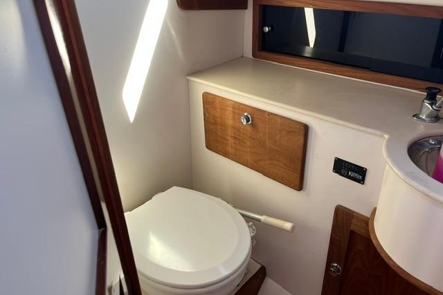 Compact bathroom in a 2006 Morris 36 boat, featuring a toilet and wooden cabinetry.