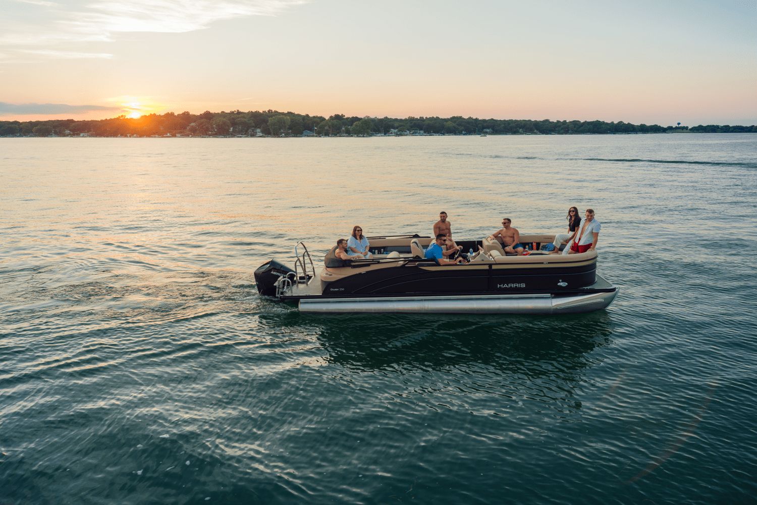 A Harris Cruiser 230 pontoon boat cruises on a calm lake at sunset.