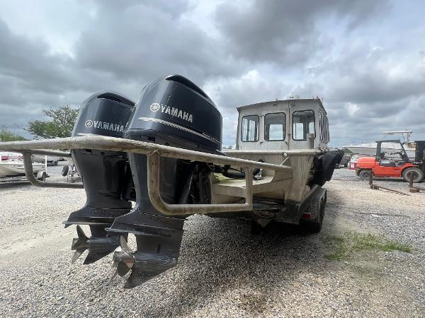 Custom Flat 28 Cabin Boat with dual Yamaha engines, parked on gravel under cloudy skies.