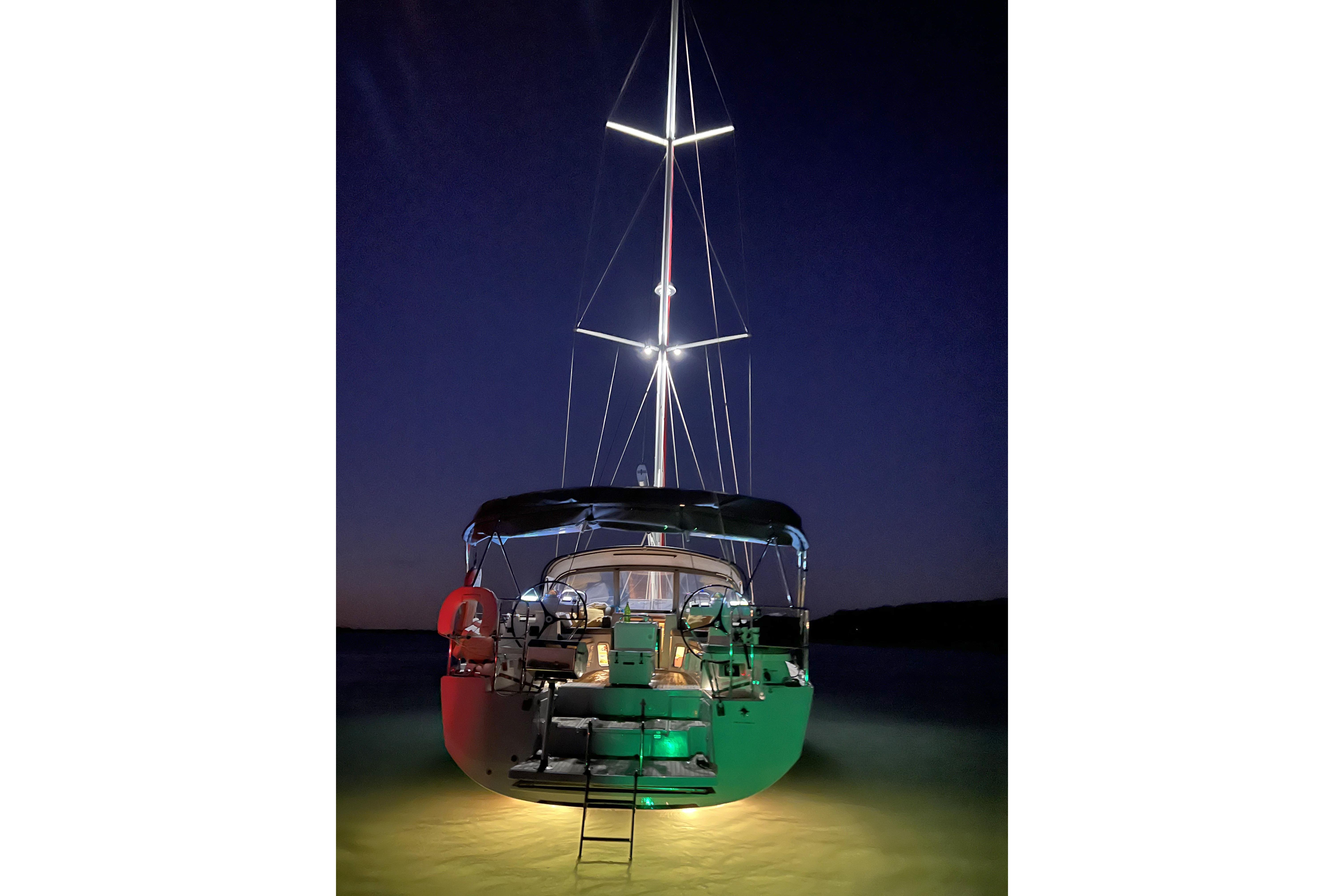 Sailing yacht Jeanneau 51, 2018 model, illuminated at night on calm waters.