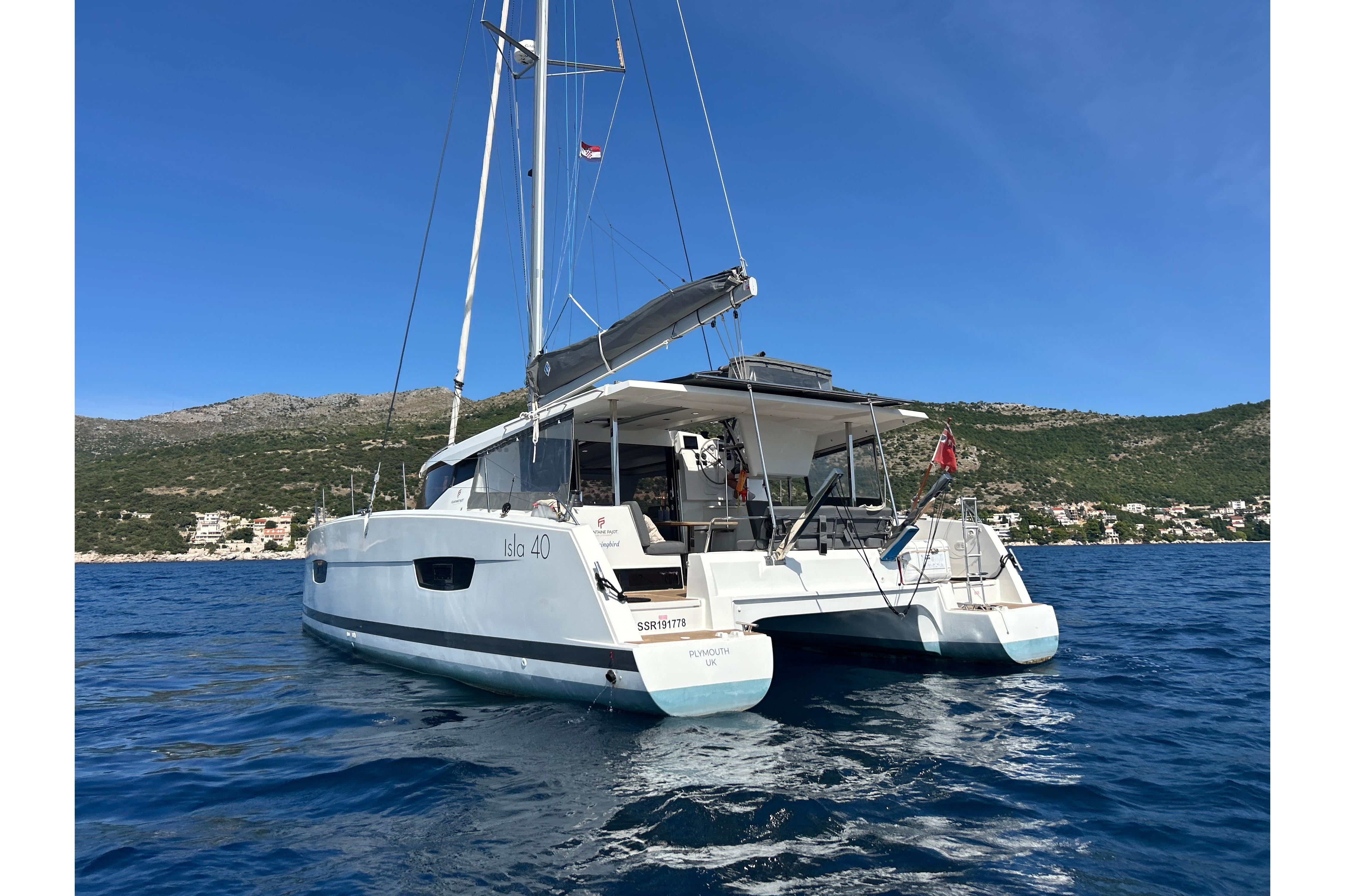 2021 Fountaine Pajot Isla 40 catamaran sailing on blue ocean near coastal landscape.