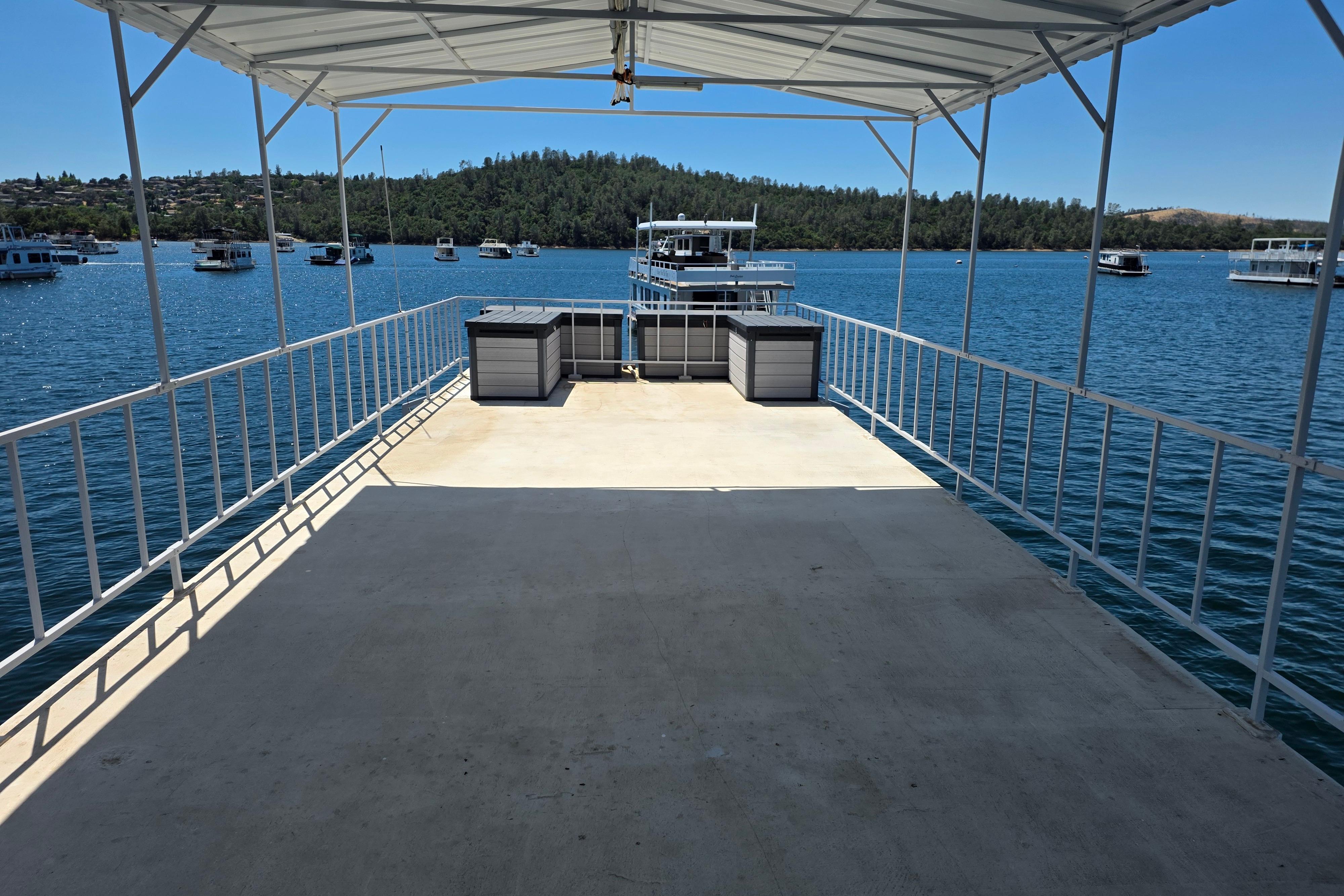 Open deck of a 2007 custom houseboat on a serene lake with distant boats.