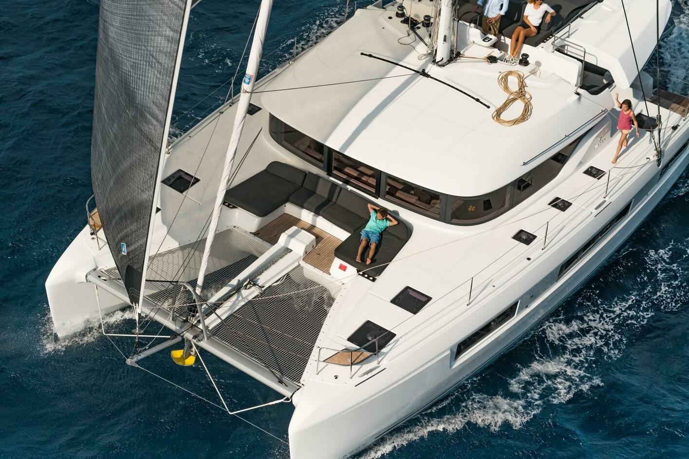 2023 Lagoon 50 catamaran sailing on blue ocean with passengers relaxing on deck.
