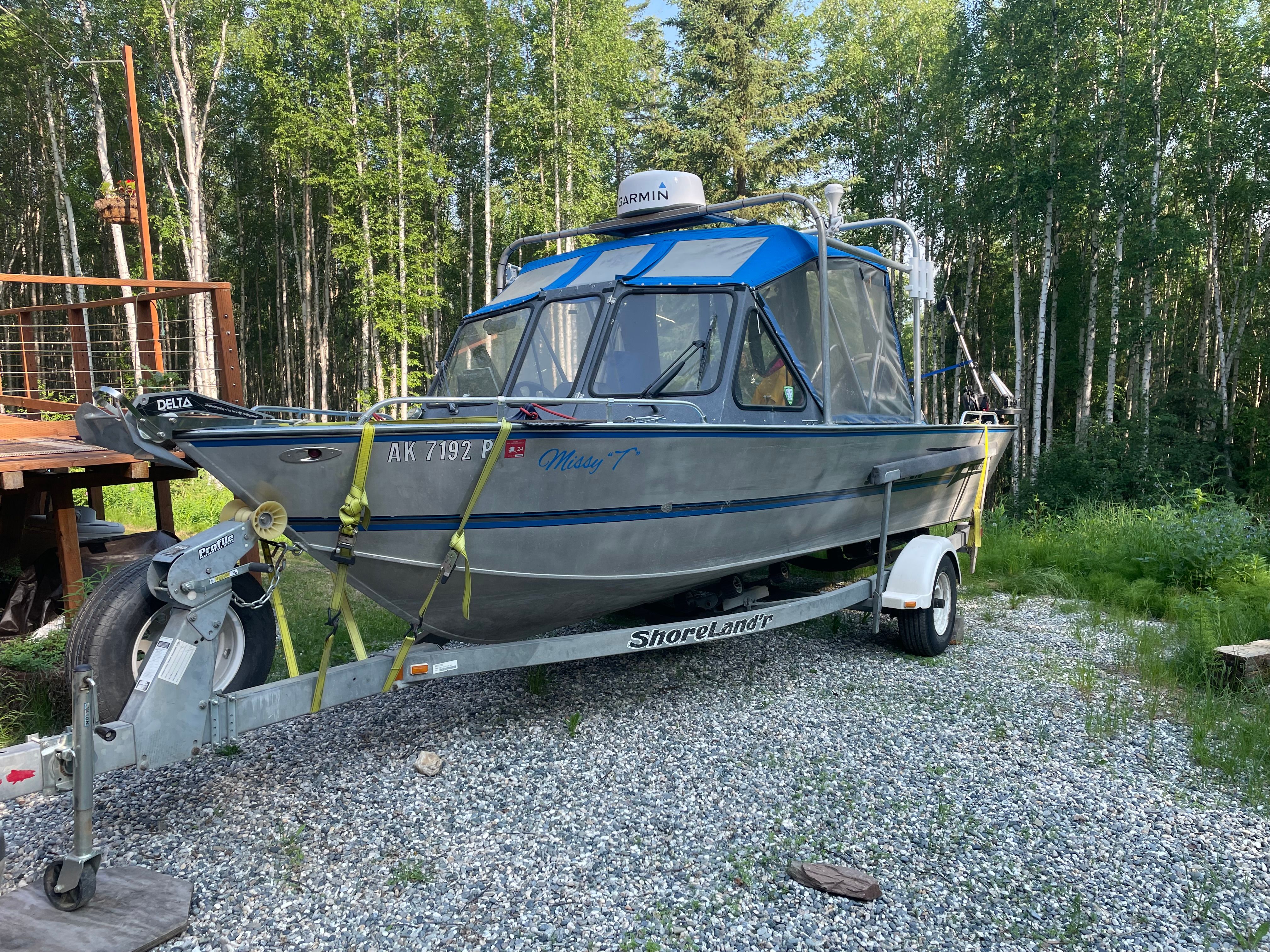 A Hewescraft Sea Runner 210 boat on a trailer, surrounded by trees.