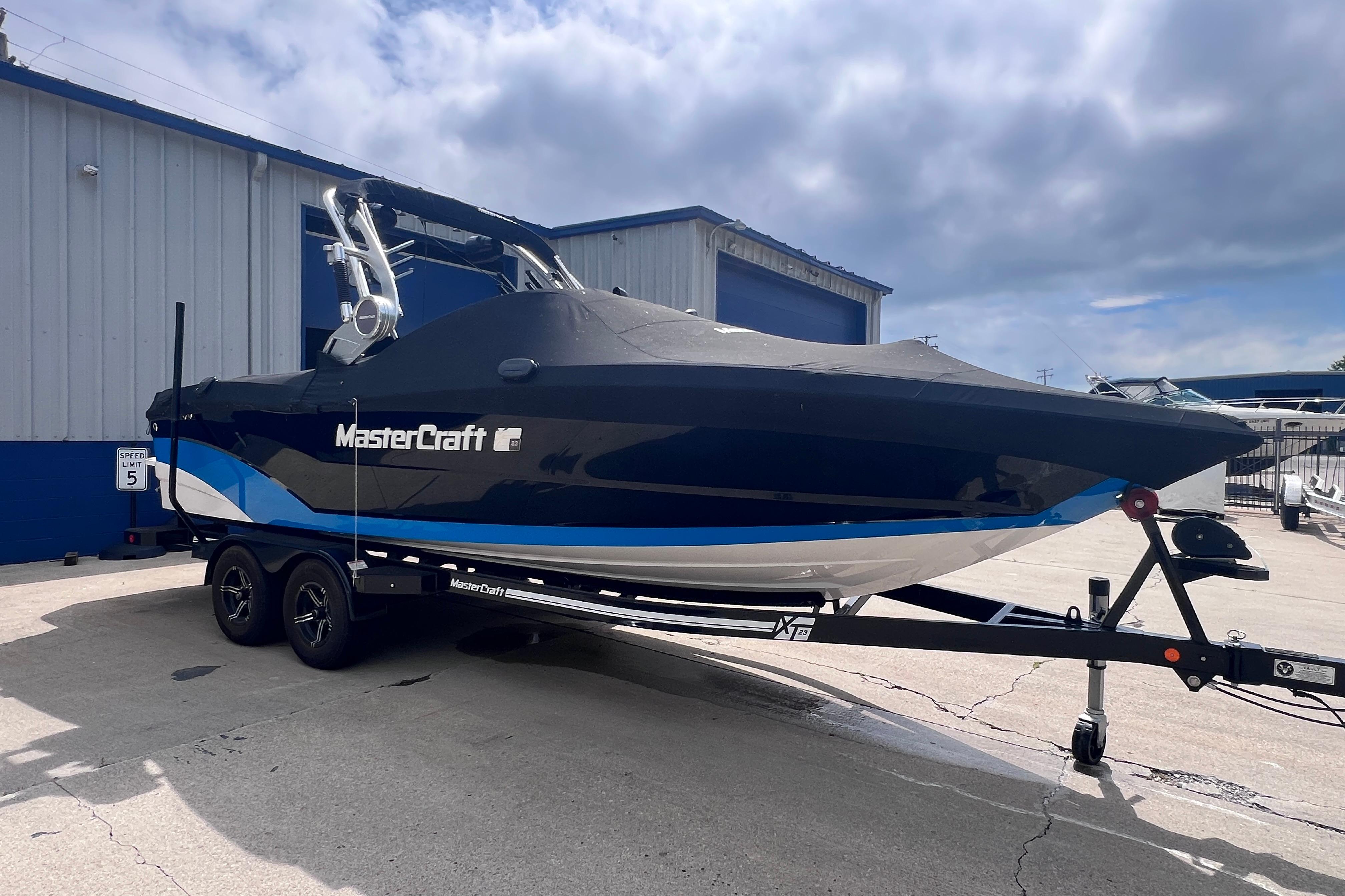 2021 MasterCraft XT23 boat on trailer, parked outside a building under cloudy sky.