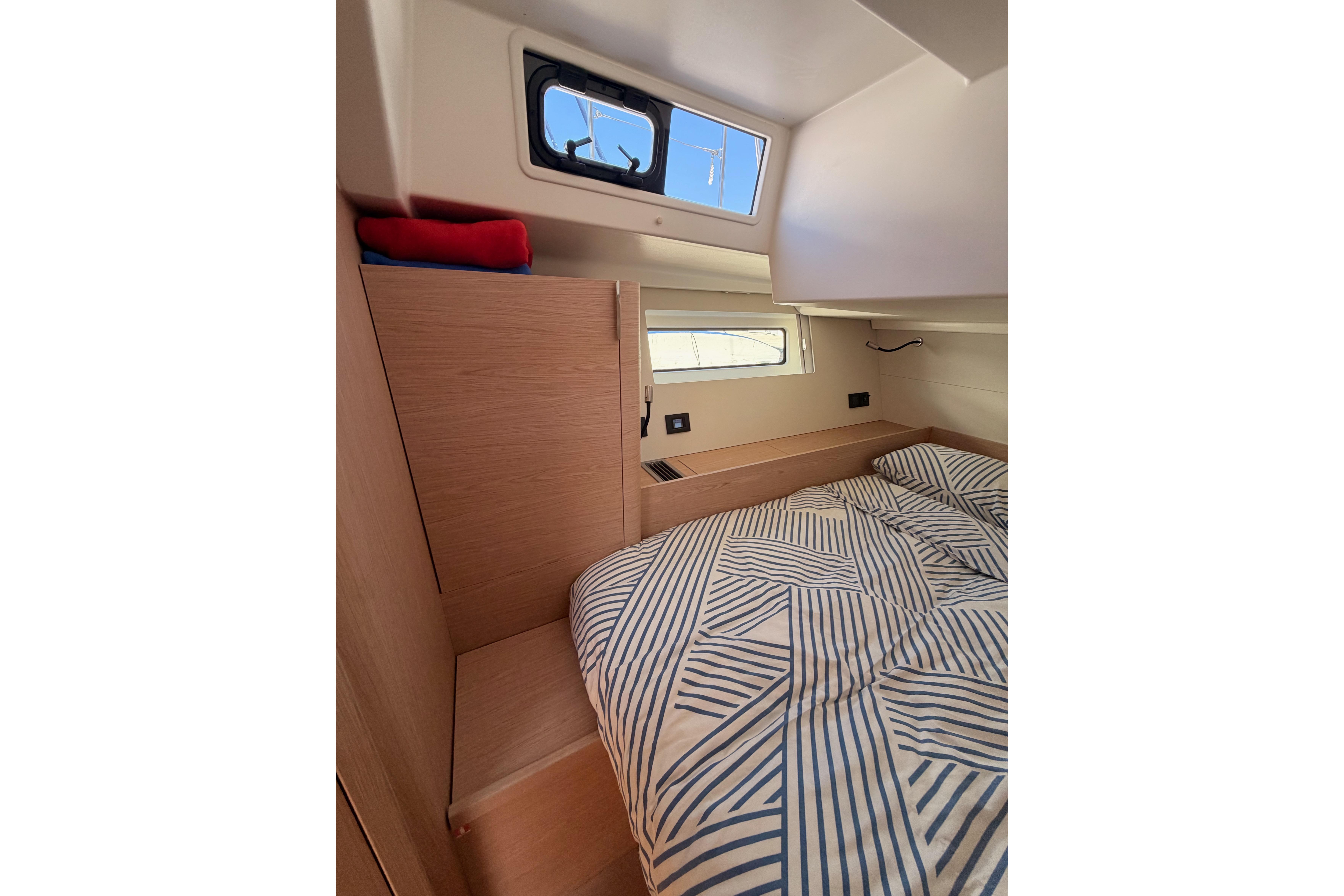 Cozy cabin interior of 2022 Beneteau Oceanis Yacht 54 with striped bedding and natural light.