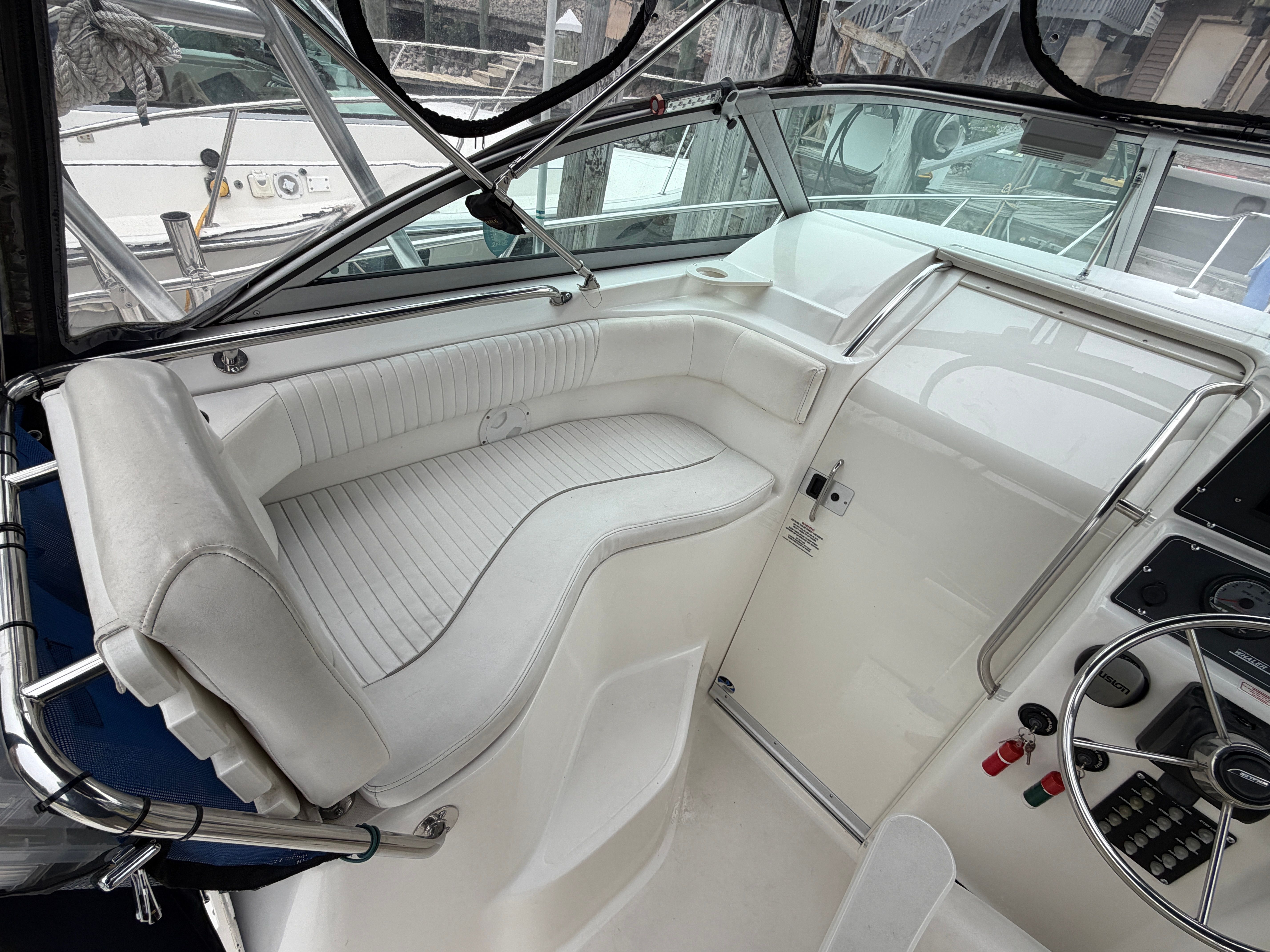 The cockpit of a 2001 Boston Whaler 26 Conquest with white upholstery and a steering console.