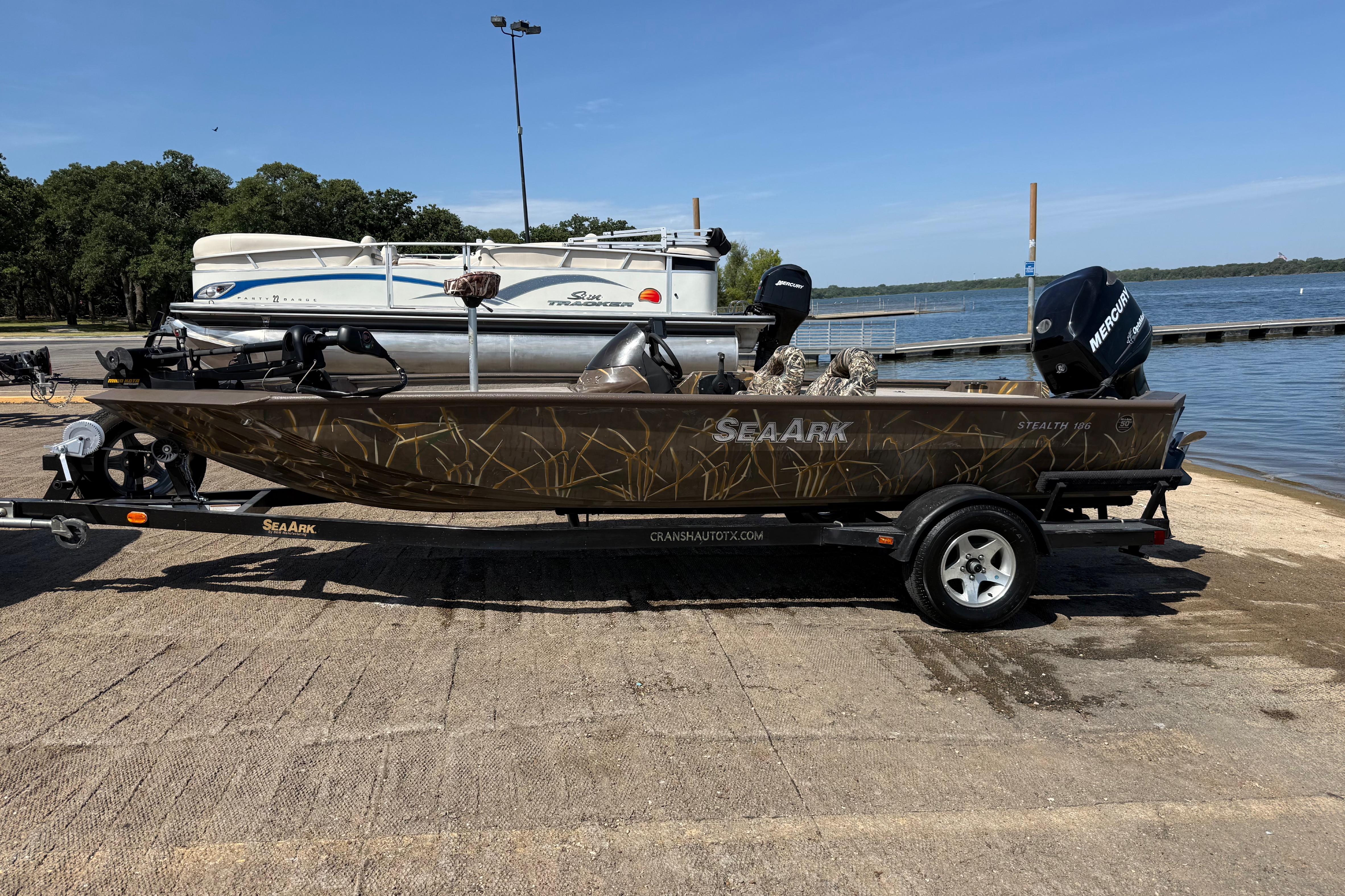 2010 SeaArk Stealth 190 boat on trailer by lakeside, featuring camouflage design and Mercury engine.
