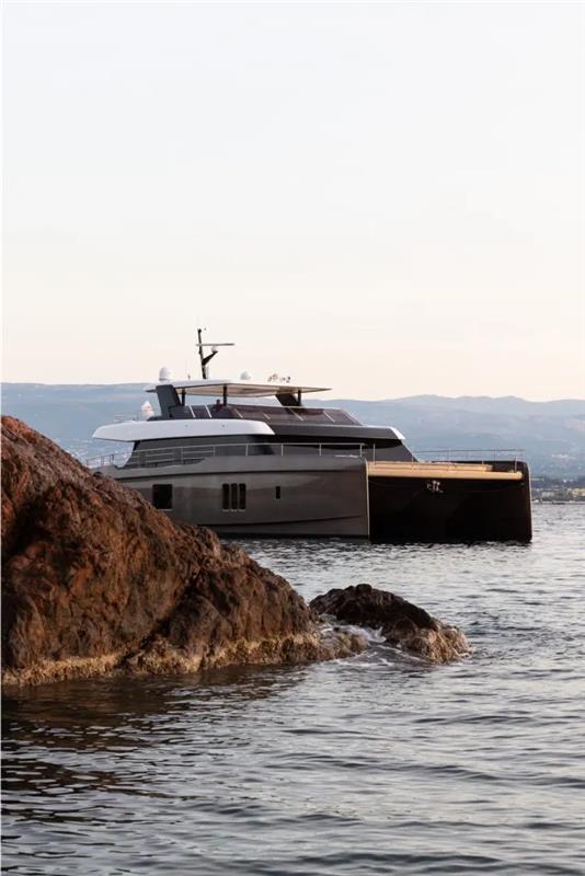 2026 Sunreef 80 Sunreef Power yacht on calm waters near rocky shore.