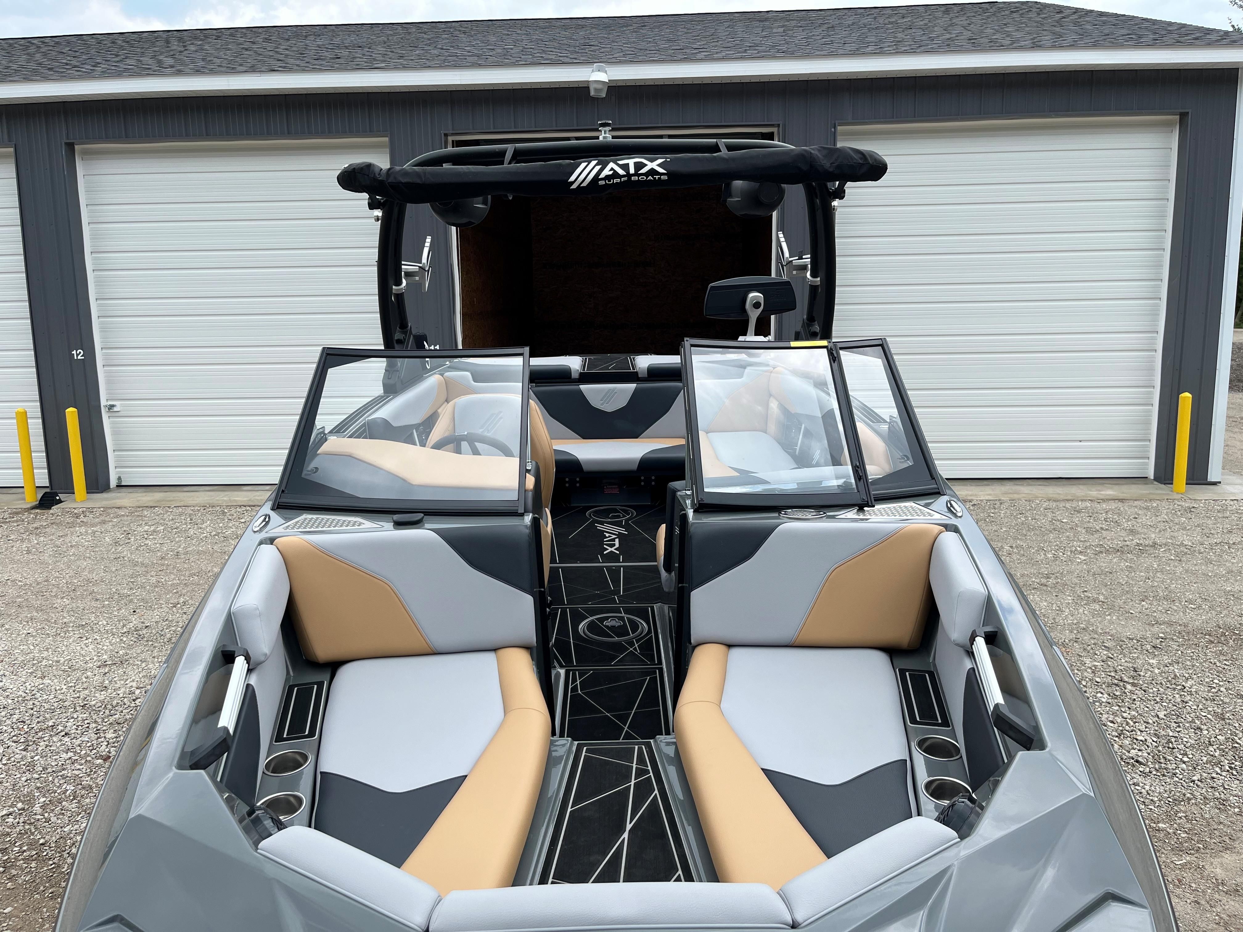 The 2022 ATX Surf Boat 22 Type-S is parked in front of a garage. It features modern seating.