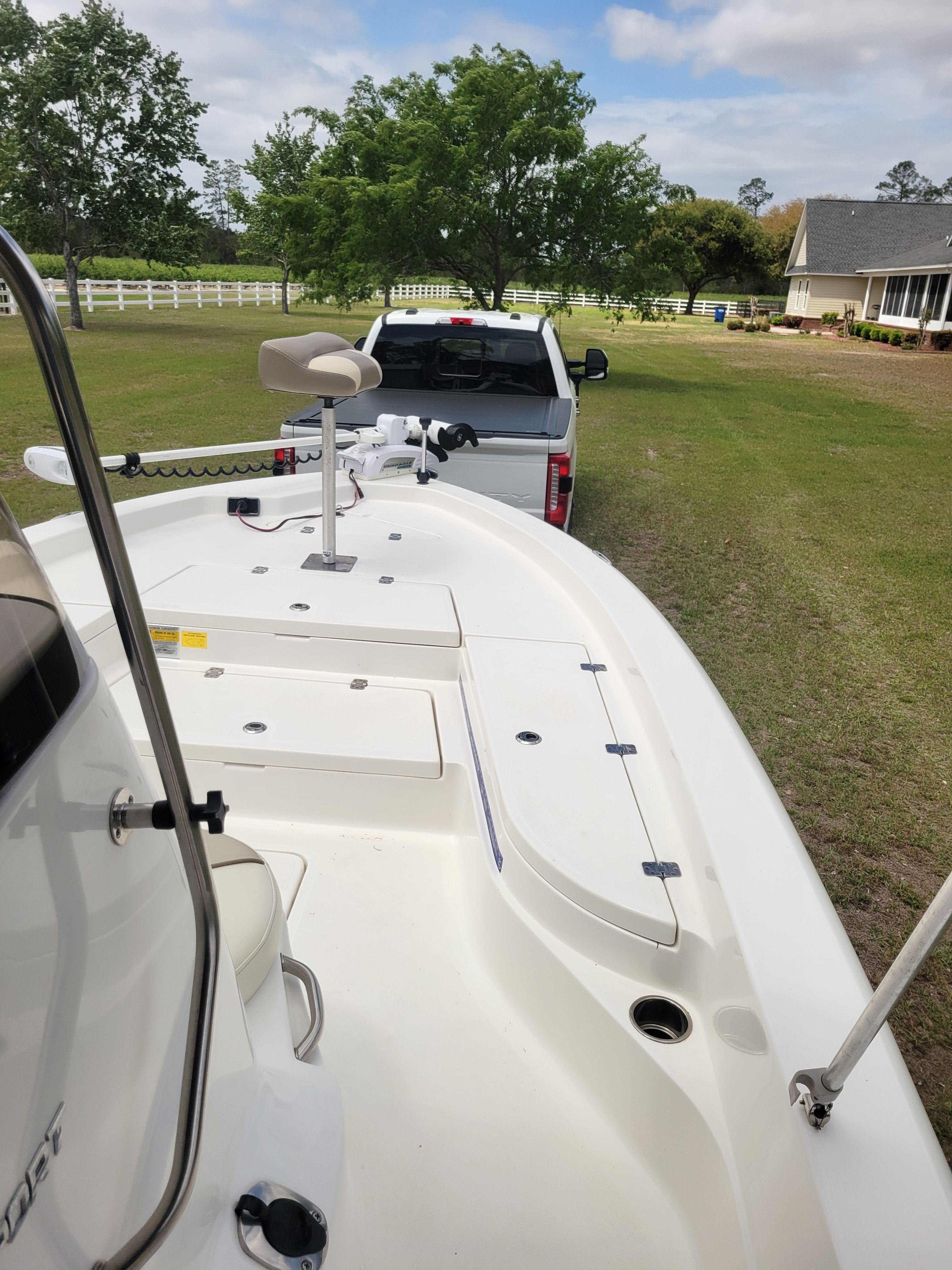 A boat on a trailer, towed by a white truck on a grassy field.