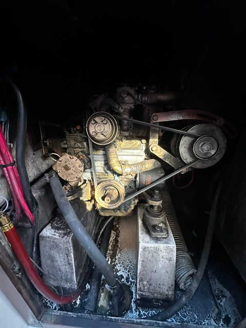 An engine compartment with an old engine, hoses, and belts in a dark area.