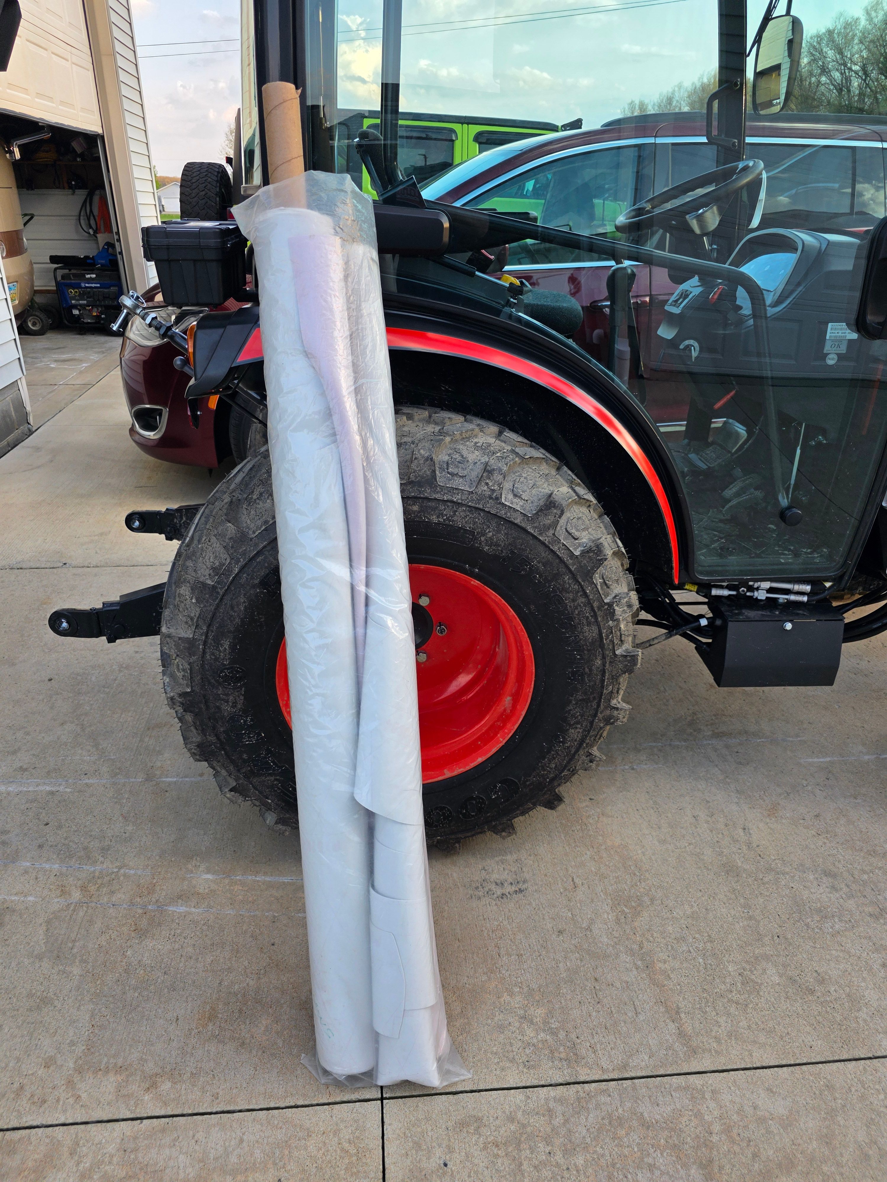 Tractor with red wheels and rolled-up material beside it.