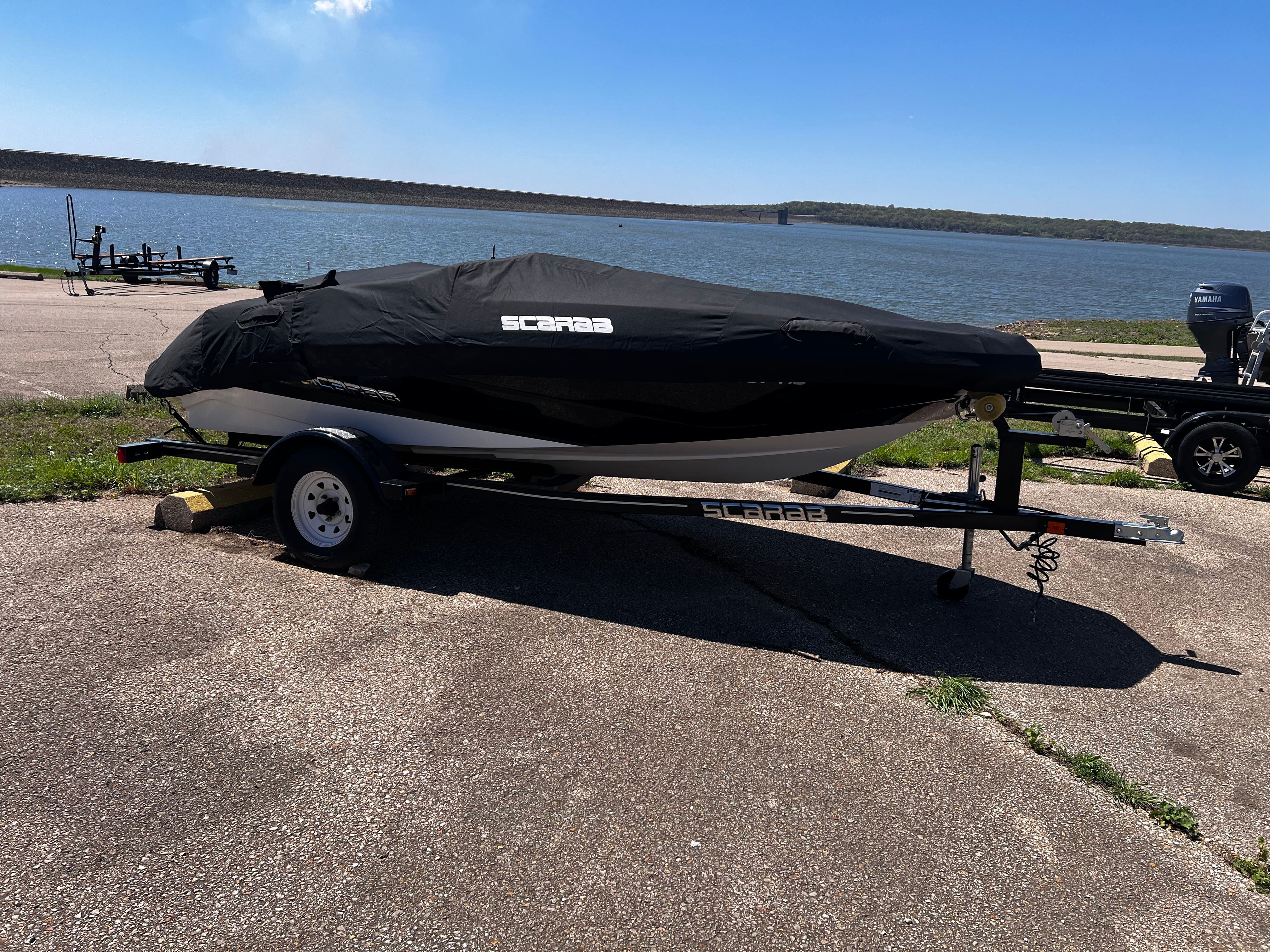 A 2019 Scarab 165 G boat on a trailer near a body of water.