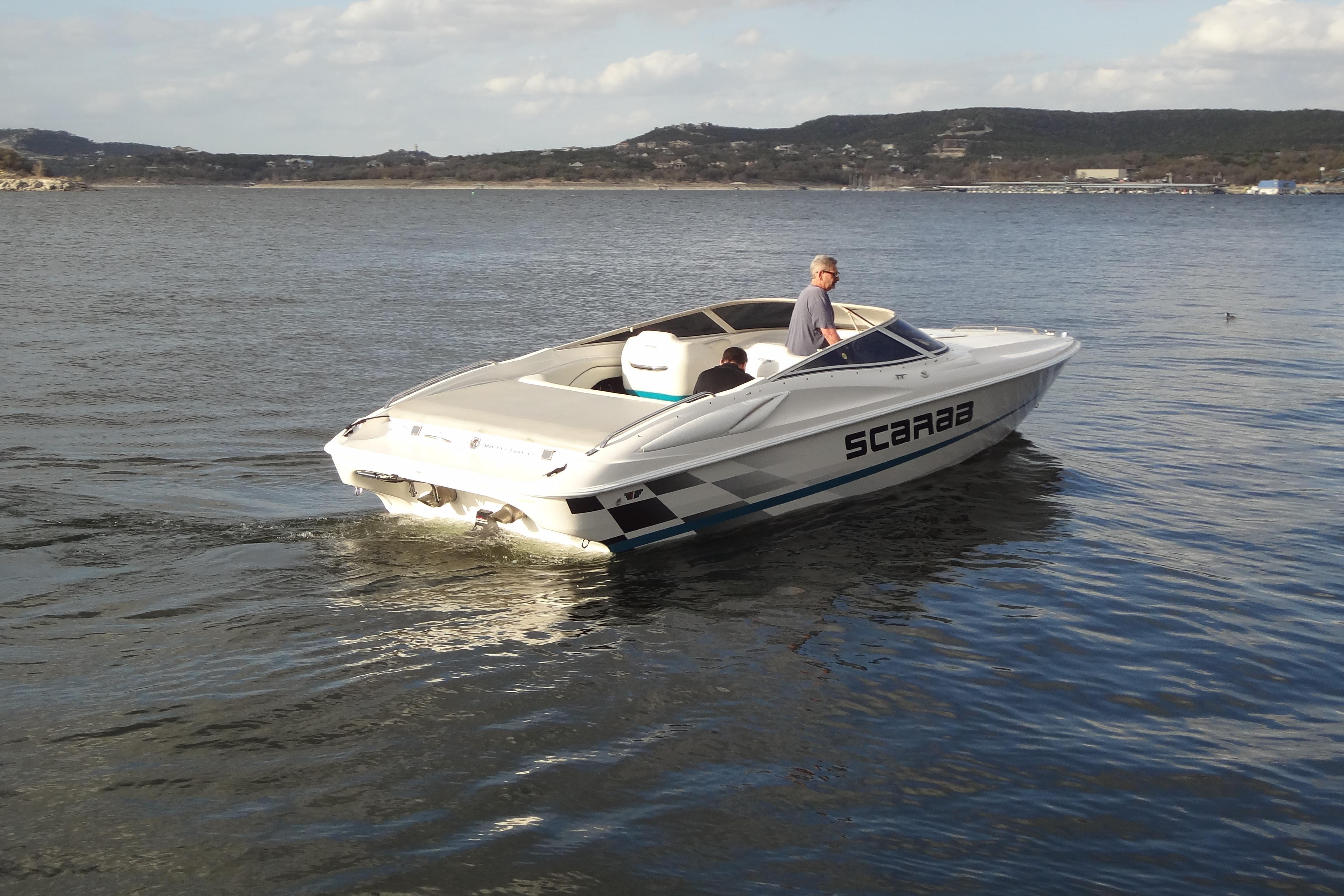 1998 Wellcraft 26 Scarab boat cruising on a calm lake with scenic hills in the background.