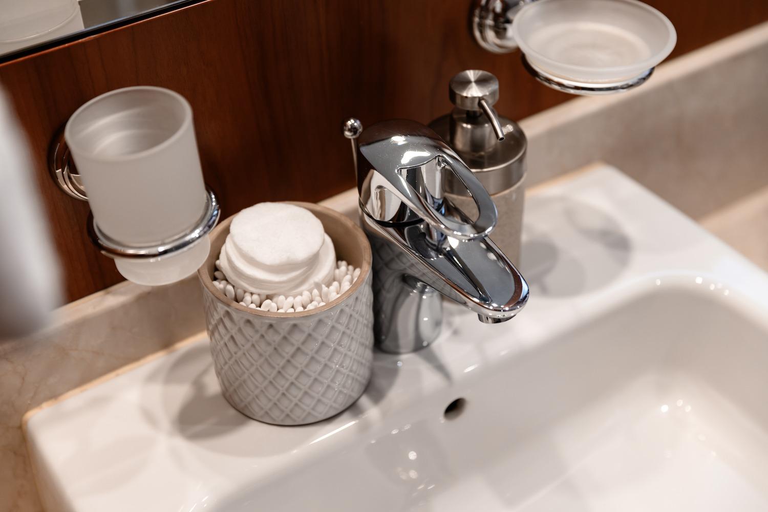 Modern bathroom sink with chrome faucet, soap dispenser, and cotton pads in a decorative holder.