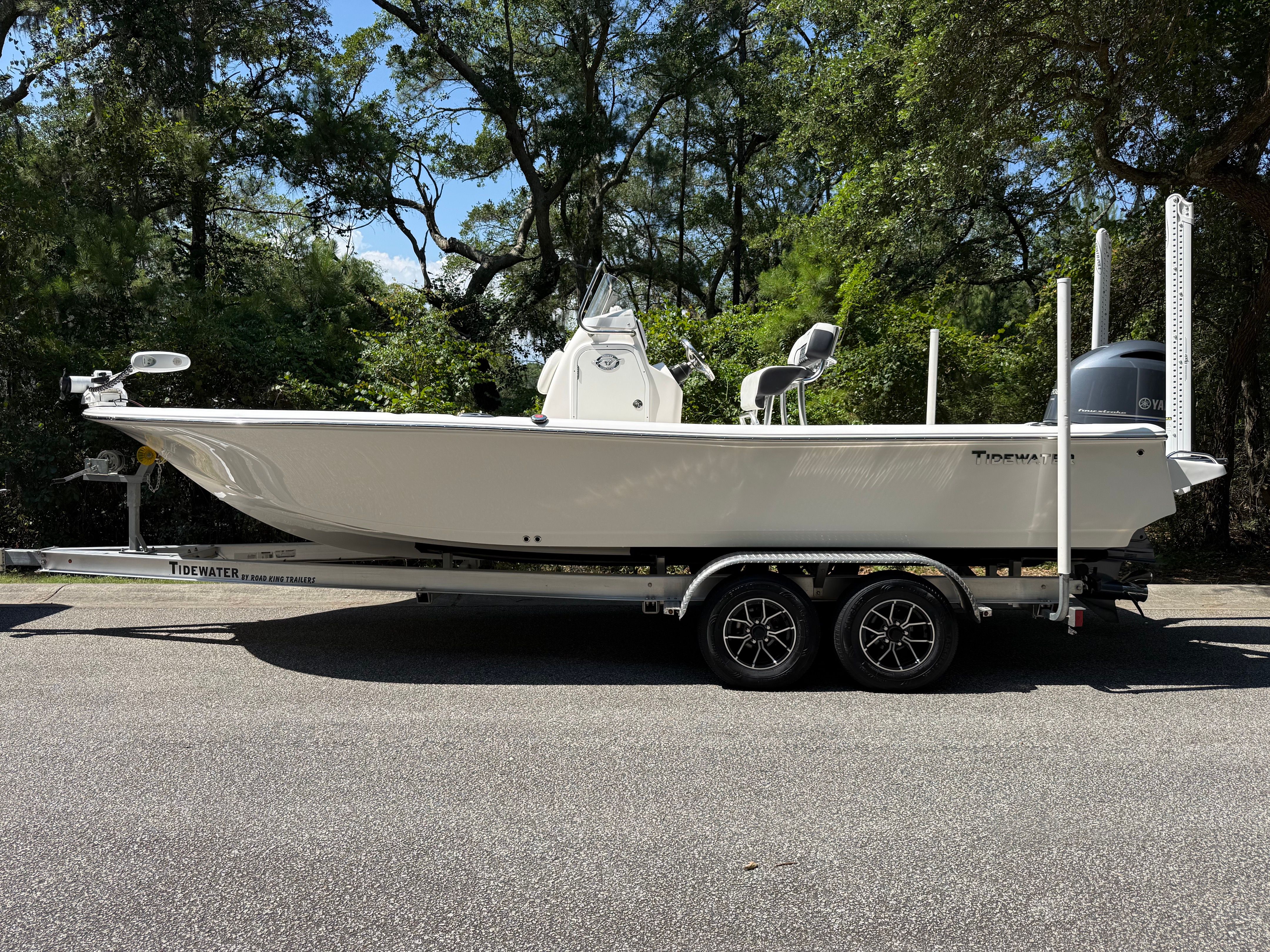 A white boat on a trailer, surrounded by trees, featuring an outboard motor.